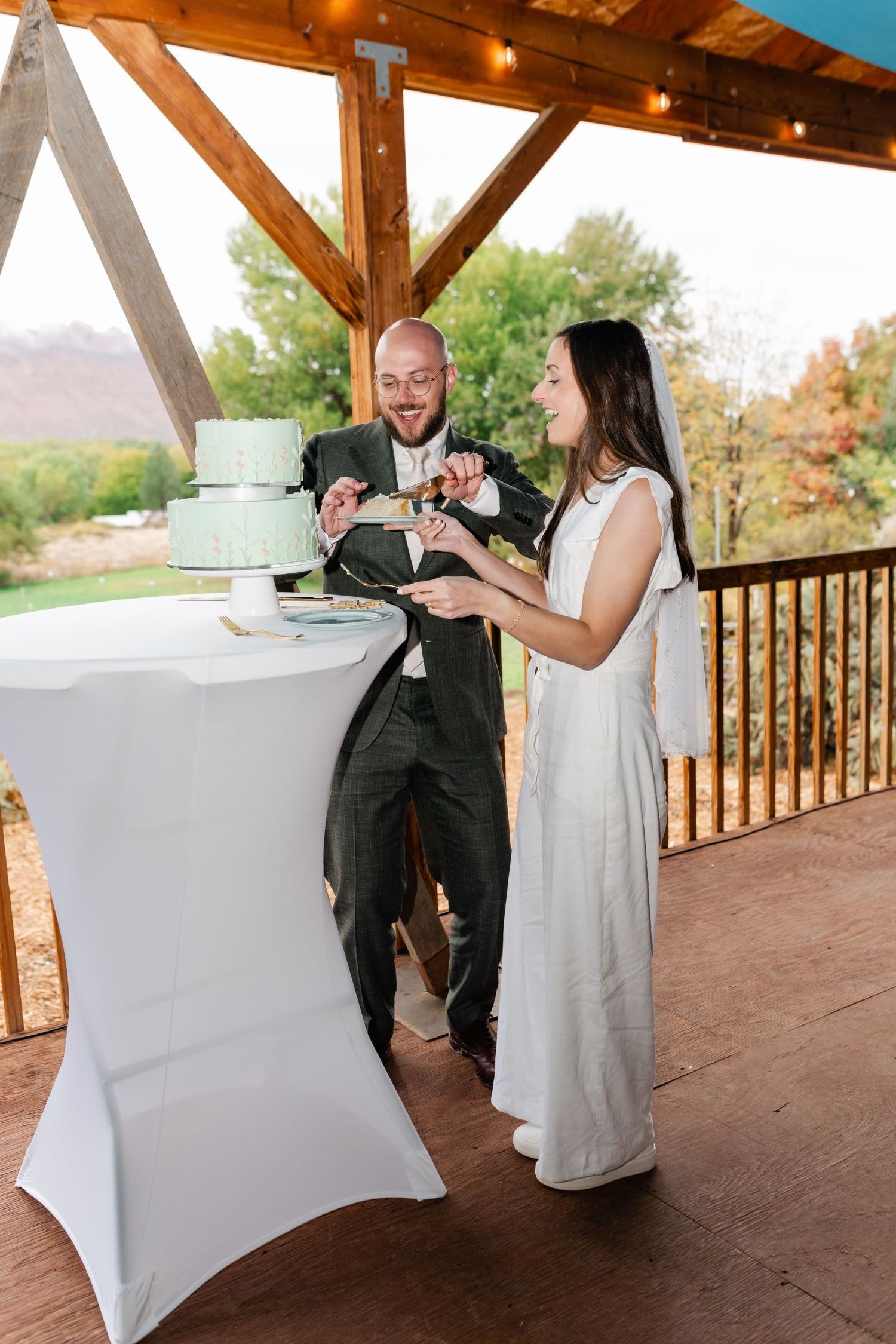 A couple enjoying their wedding cake together at a reception on an outdoor covered deck.