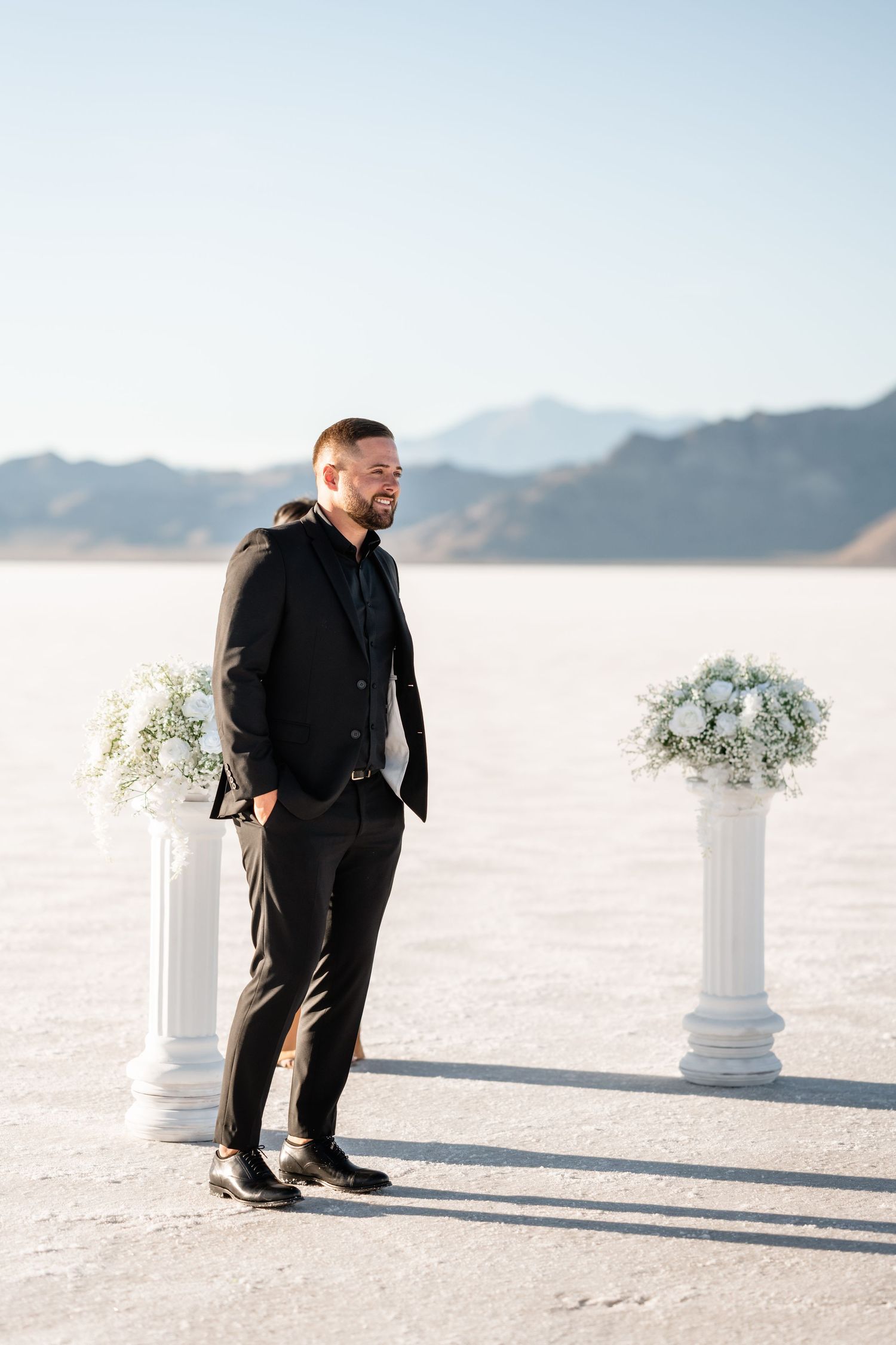 Wedding ceremony setup on salt flats with white pedestals and floral arrangements against mountain backdrop.