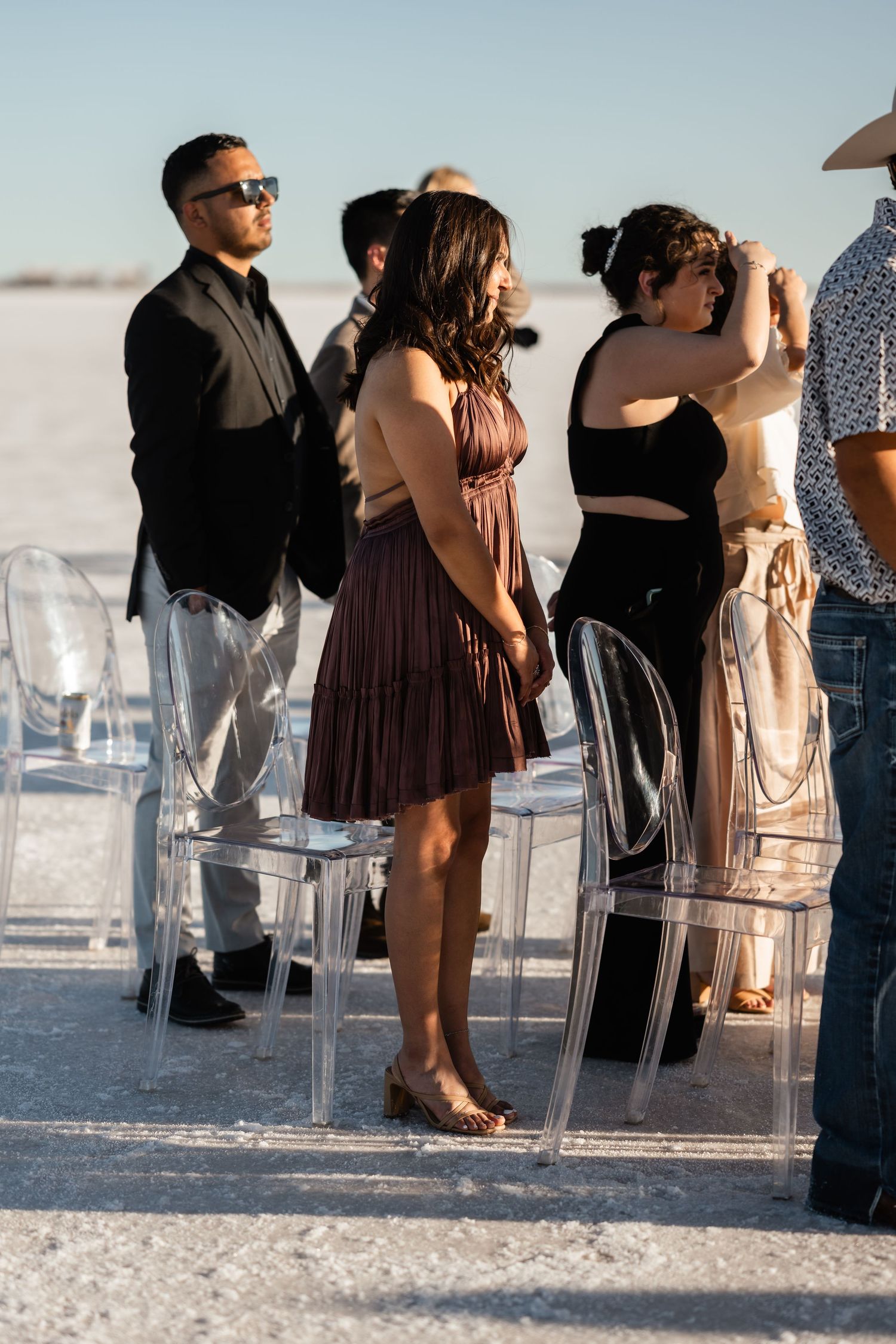 Clear acrylic chairs set up for wedding ceremony on bright white salt flats.
