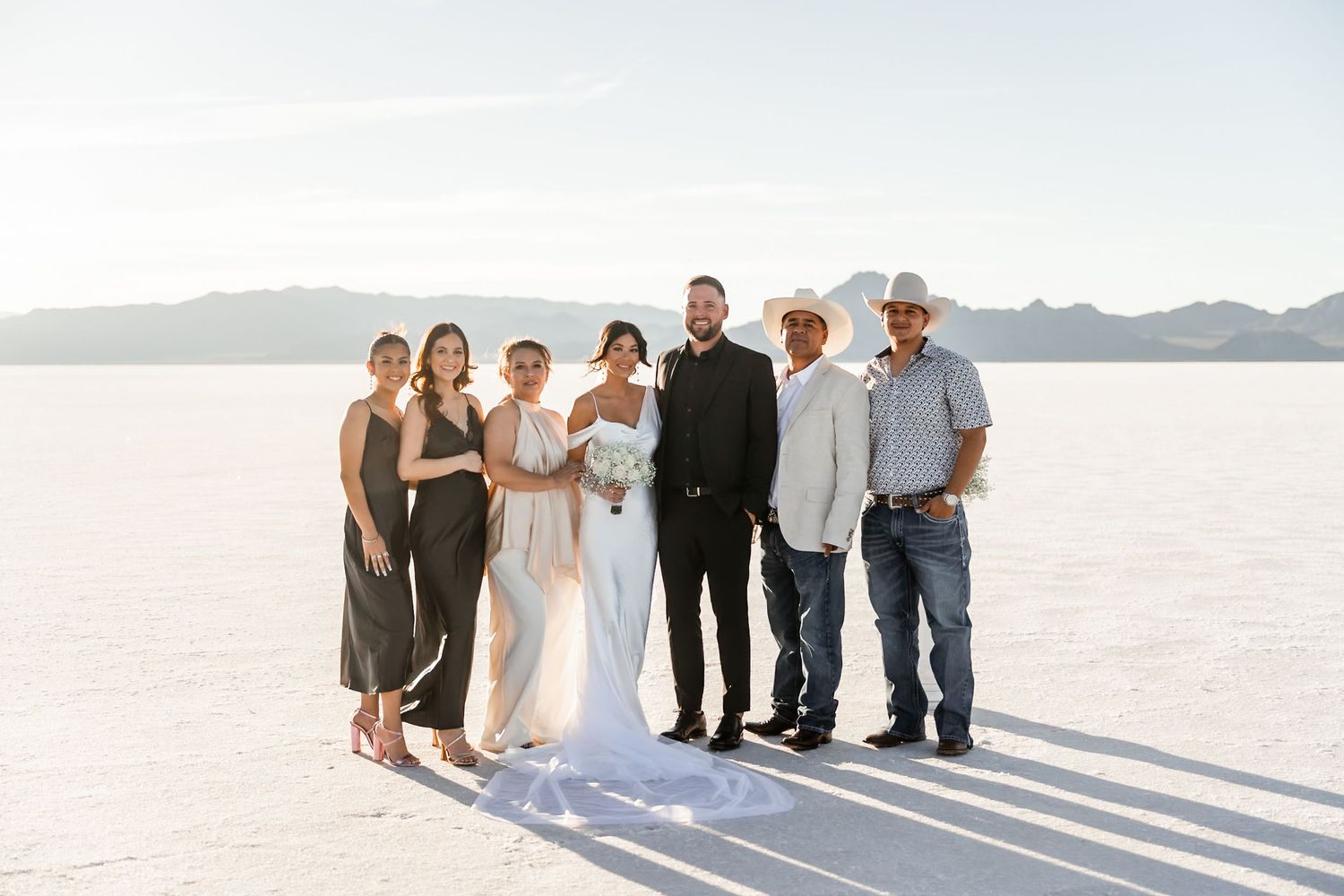Wedding party posing for photos on bright salt flats with mountain range in background.