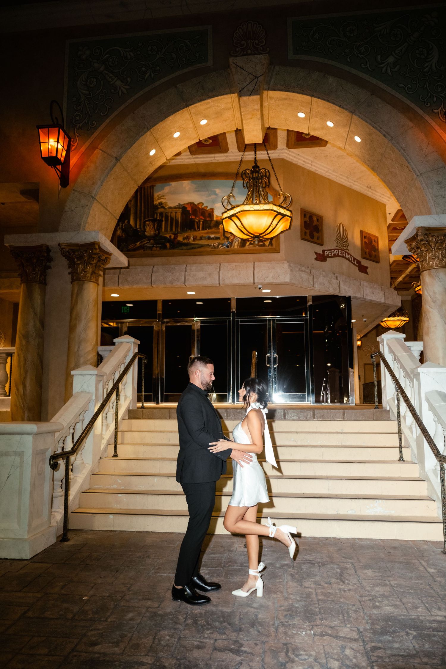 A couple dancing on an elegant stone staircase beneath an illuminated archway with ornate architectural details.