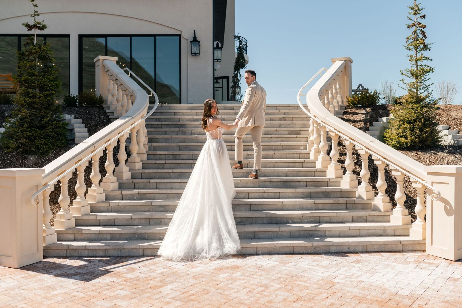 Wedding couple walks up an elegant stone staircase at Siempre wedding venue with a bridal gown in view. Luxury Wedding Photographer.