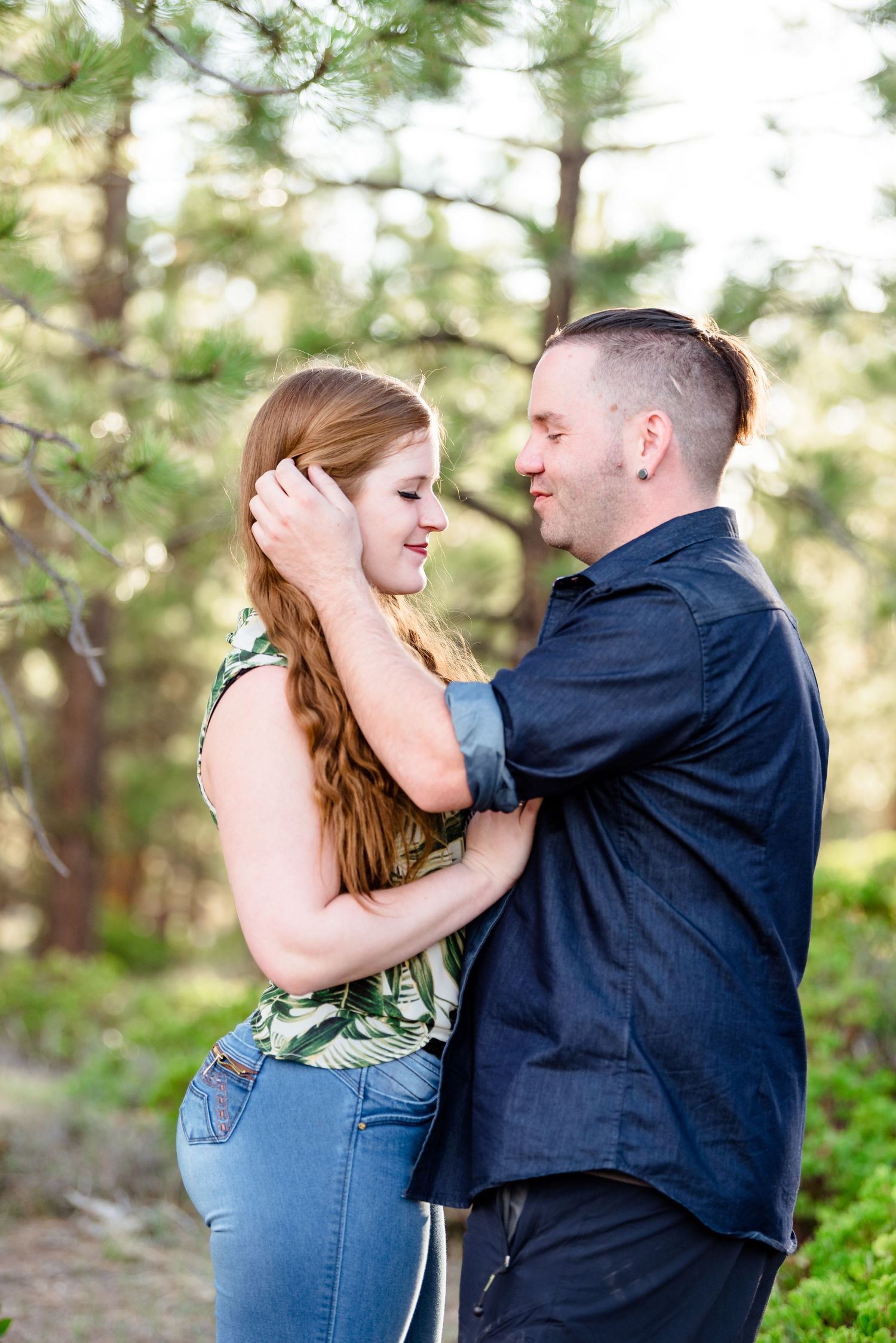 A couple shares a romantic embrace in a sunlit forest setting with pine trees in the background. Bryce Canyon Photographer.