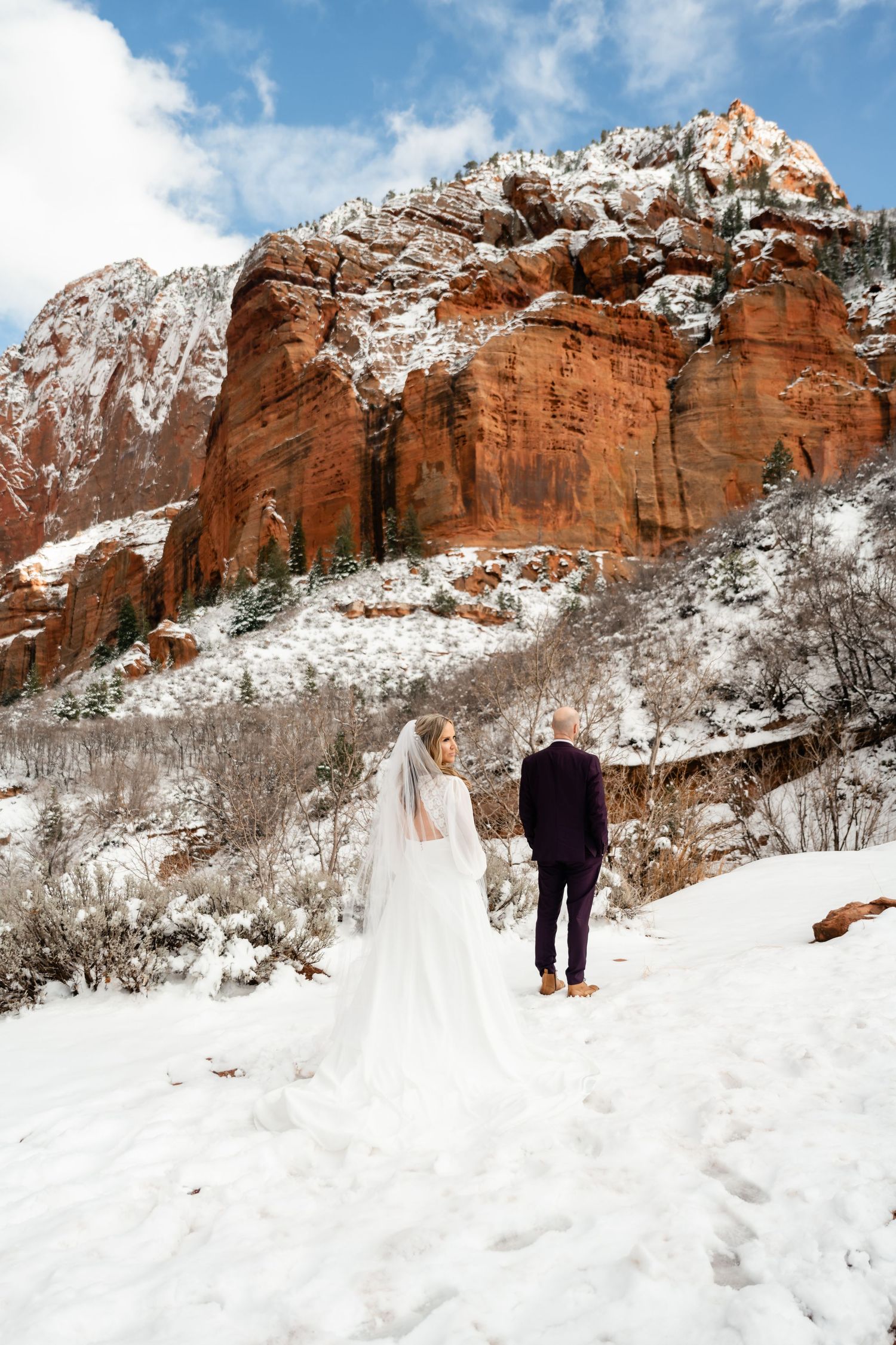 A winter wedding photoshoot against snow-covered red rock cliffs in a dramatic mountain landscape.