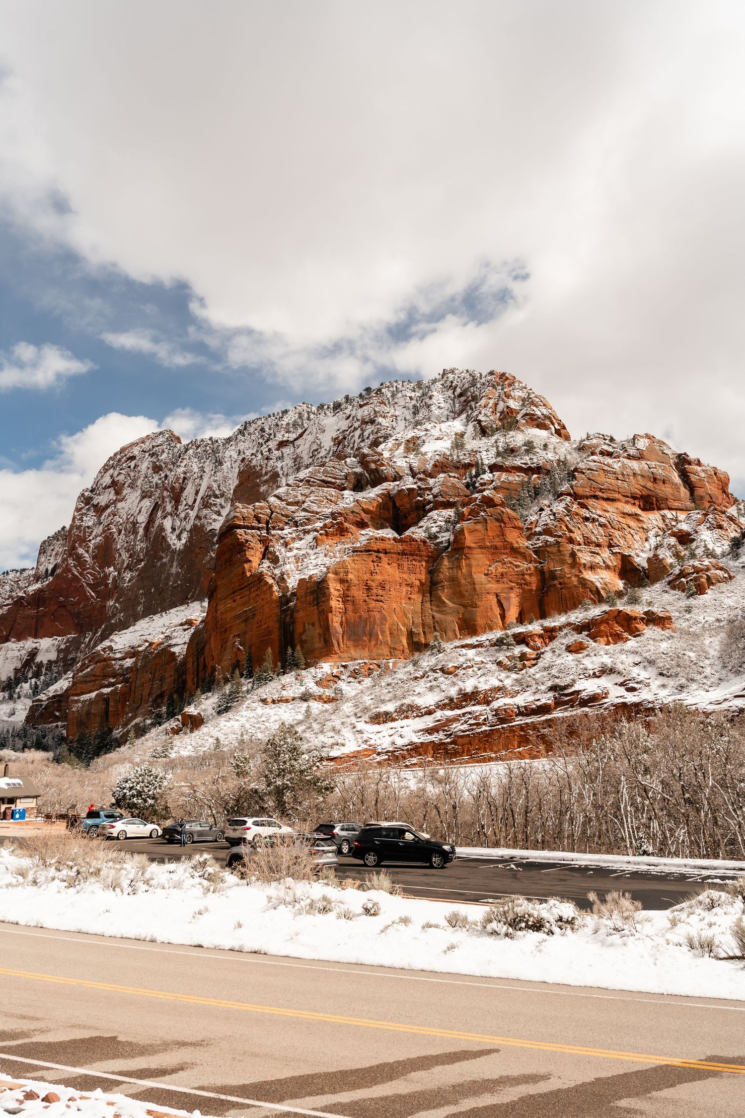 Snow-covered red rock formations along a desert highway under cloudy winter skies.