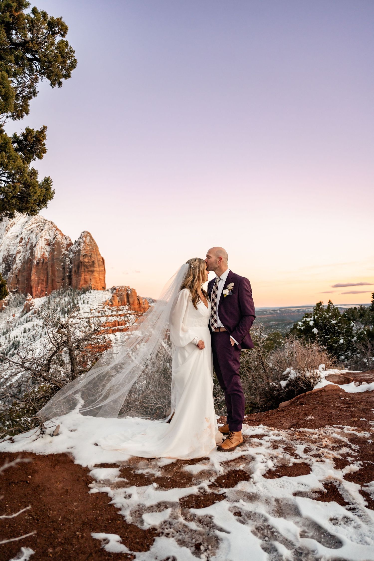 A magical winter wedding scene with snow-dusted red rocks and flowing white dress at sunset.