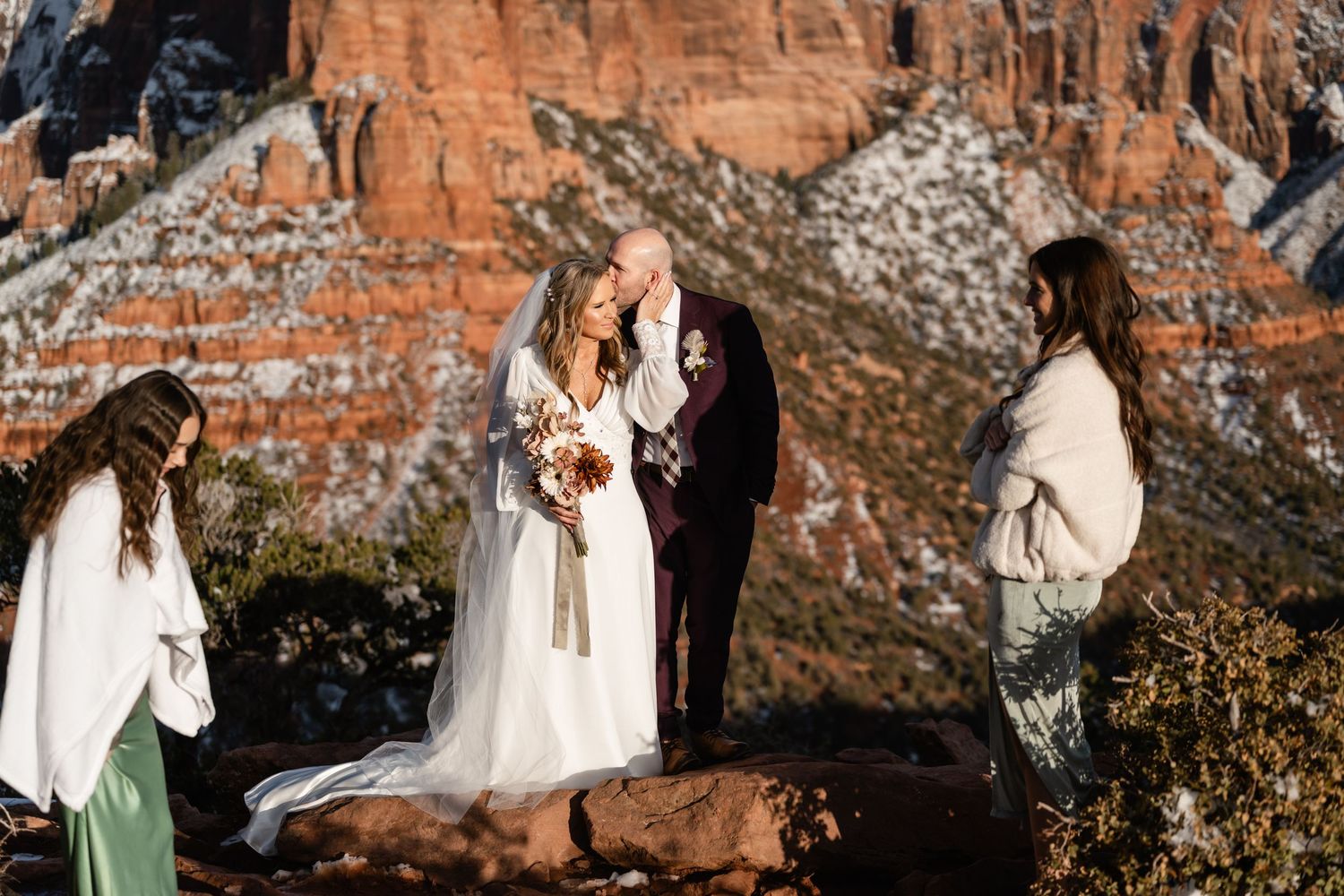 An intimate outdoor gathering against dramatic red rock cliffs on a winter day.