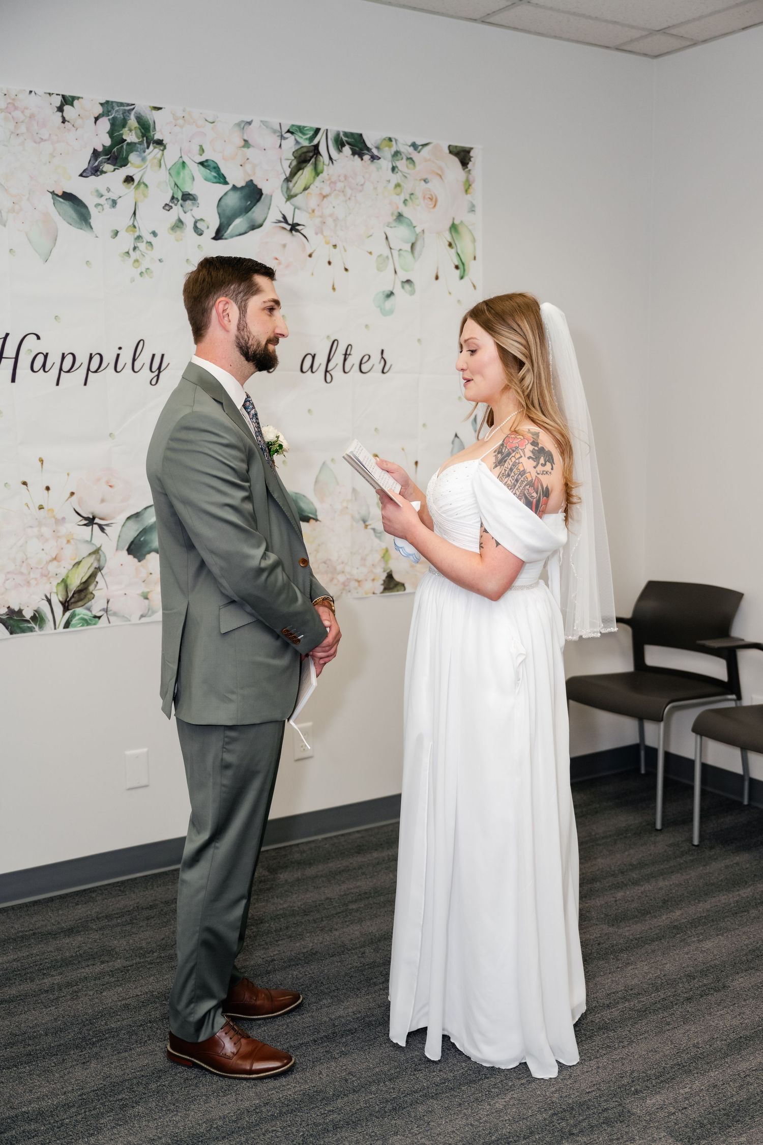 A couple shares a tender first look moment before their wedding in a modern room with floral wall decor.
