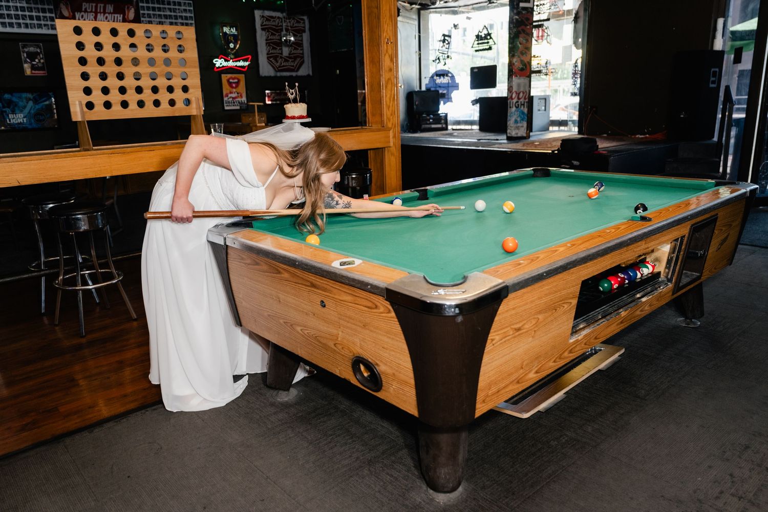 A couple in wedding attire playing pool at a casual bar setting.
