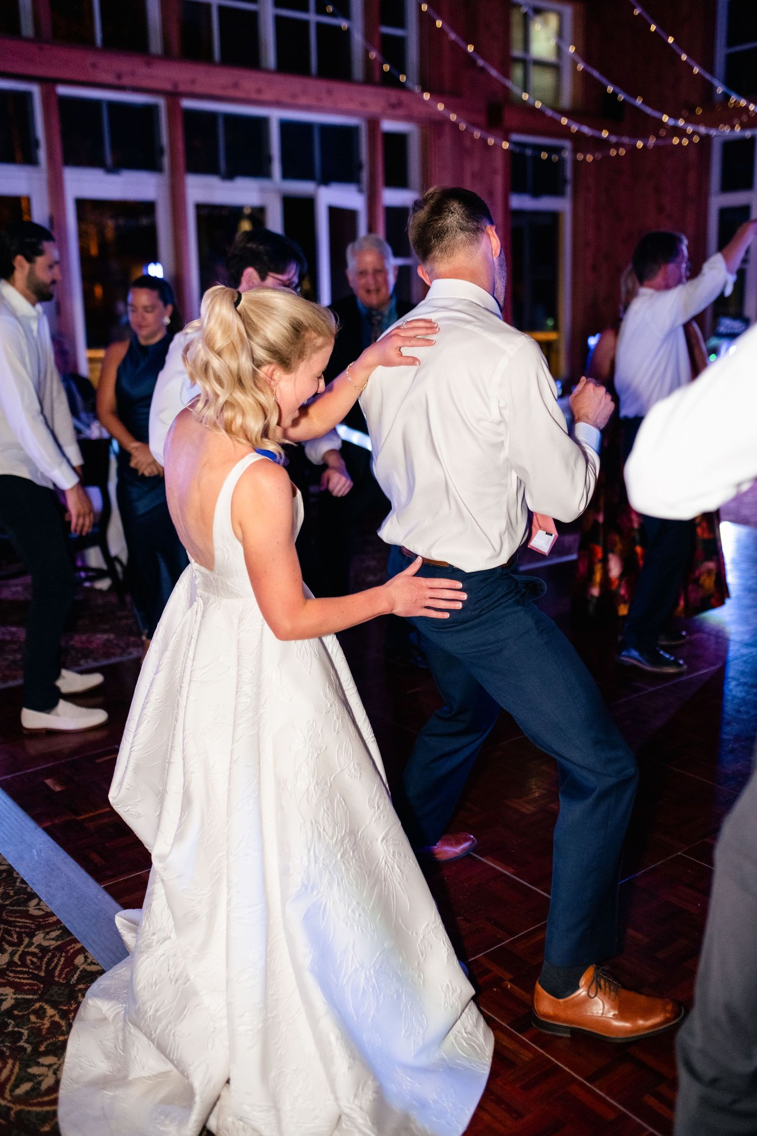 Wedding celebration with guests dancing in elegant venue with string lights.