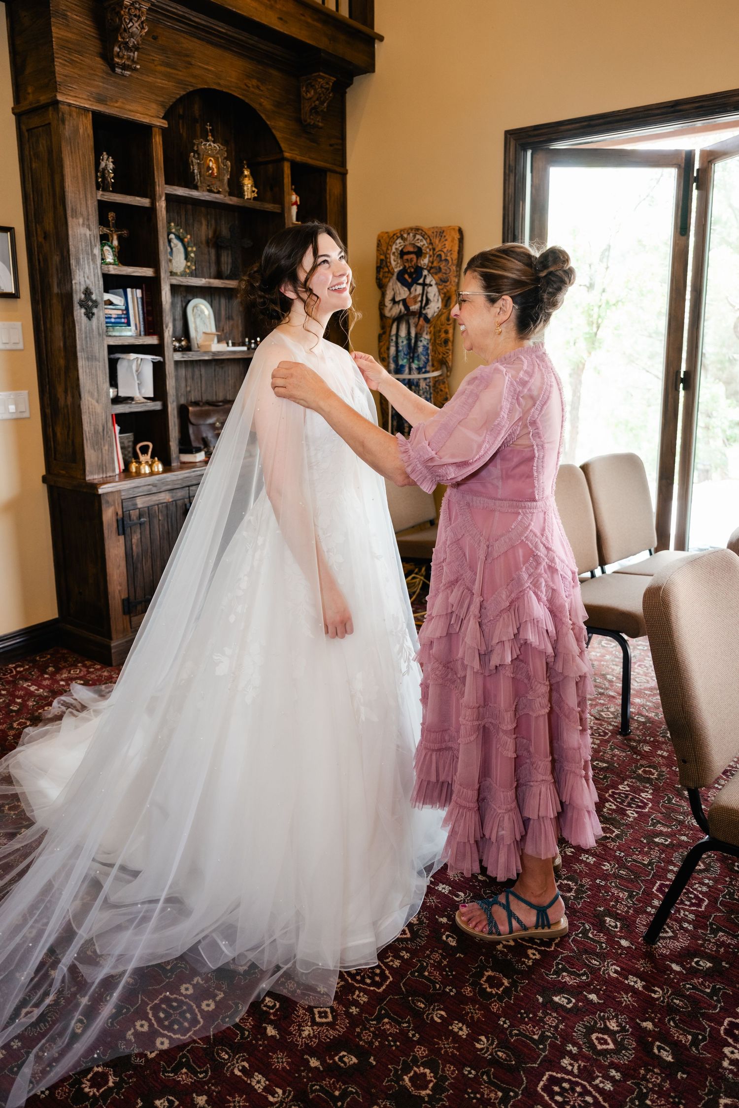 Beautiful white wedding dress being fitted and arranged on a patterned carpet.