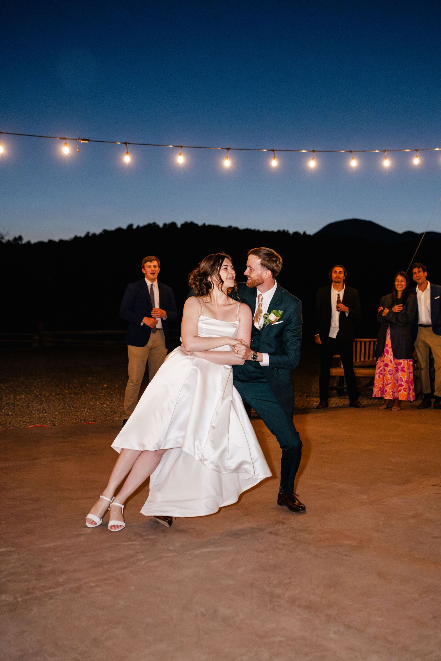 Couple shares romantic dance under string lights at outdoor wedding reception.