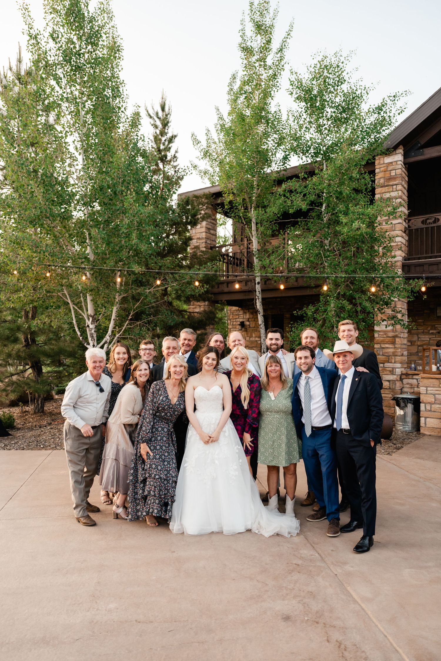 Wedding party poses for a group photo outside a rustic mountain venue with birch trees.