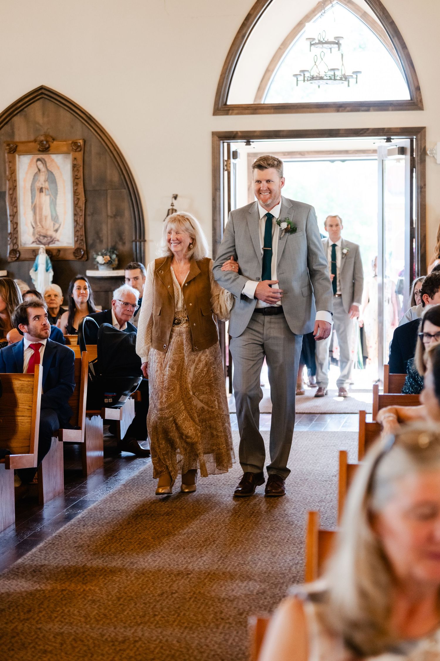 Wedding processional in church with gothic arched windows and religious artwork.