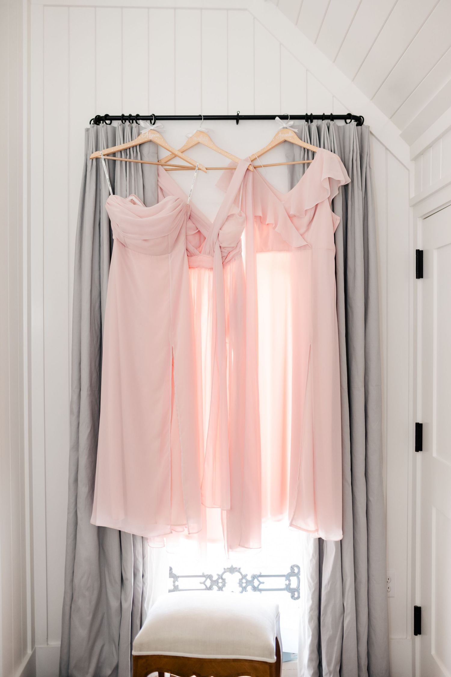 Light pink bridesmaid dresses hang on white hangers against a white wall.