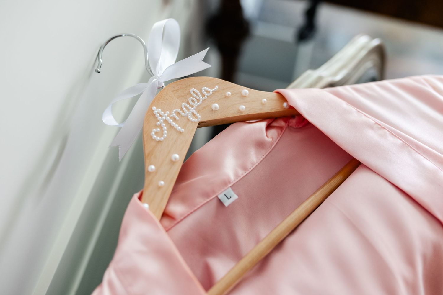 Pink silk robes hanging on wooden hangers in soft natural light.