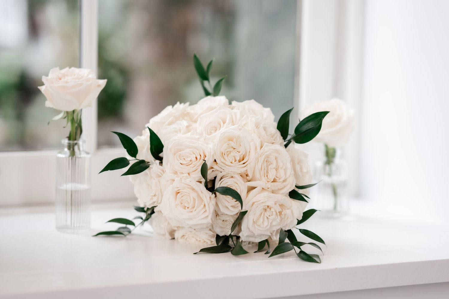 Elegant white rose and greenery wedding bouquet displayed near a window.
