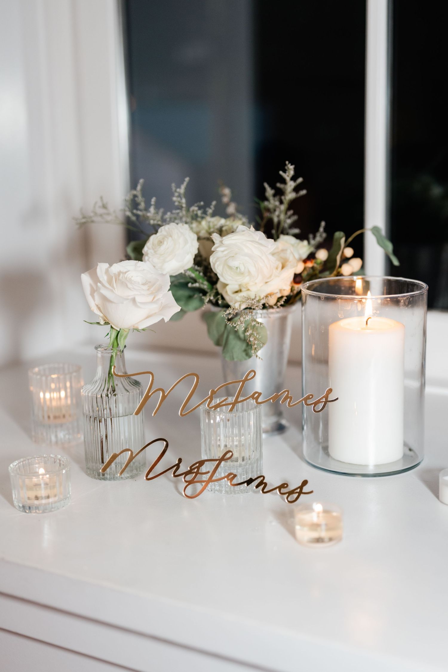 Elegant wedding table decor featuring white candles, roses and gold script name cards.