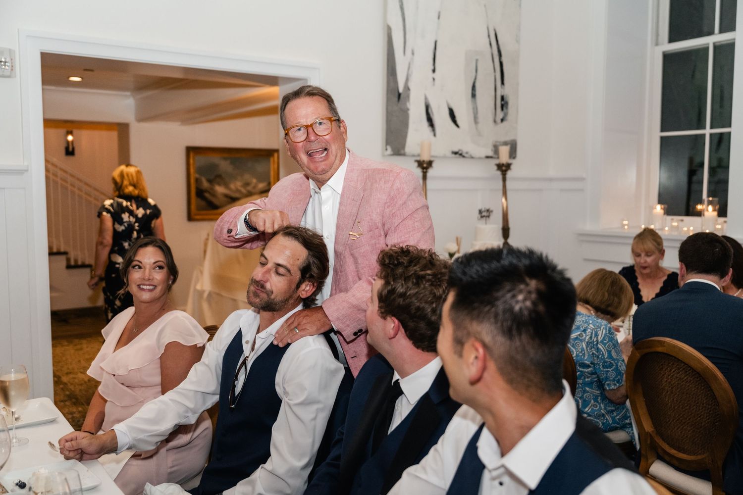 Wedding reception scene with guests celebrating and raising glasses in a bright indoor space.