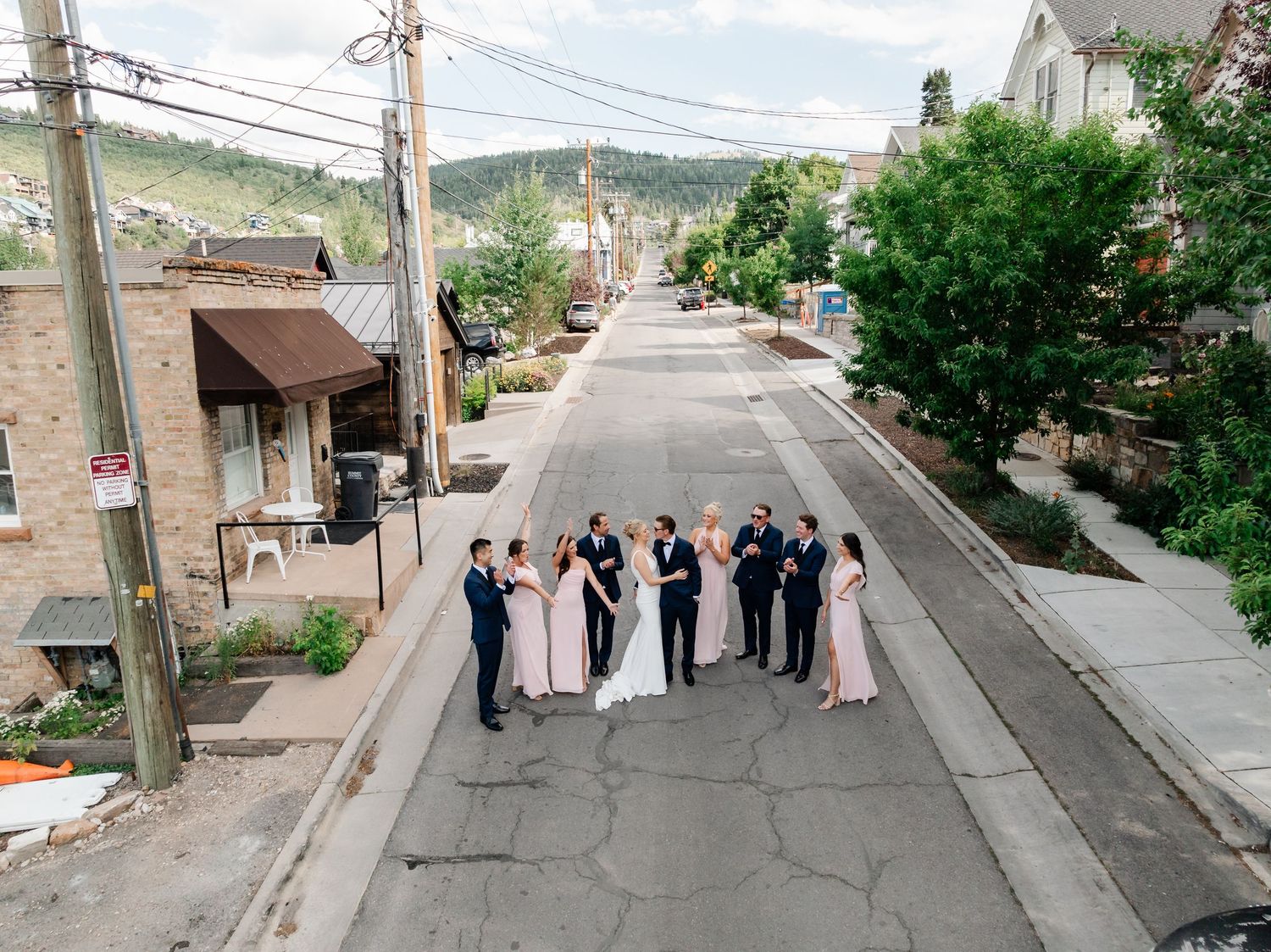 Wedding group gathered on sloped city street with mountains visible in distance.