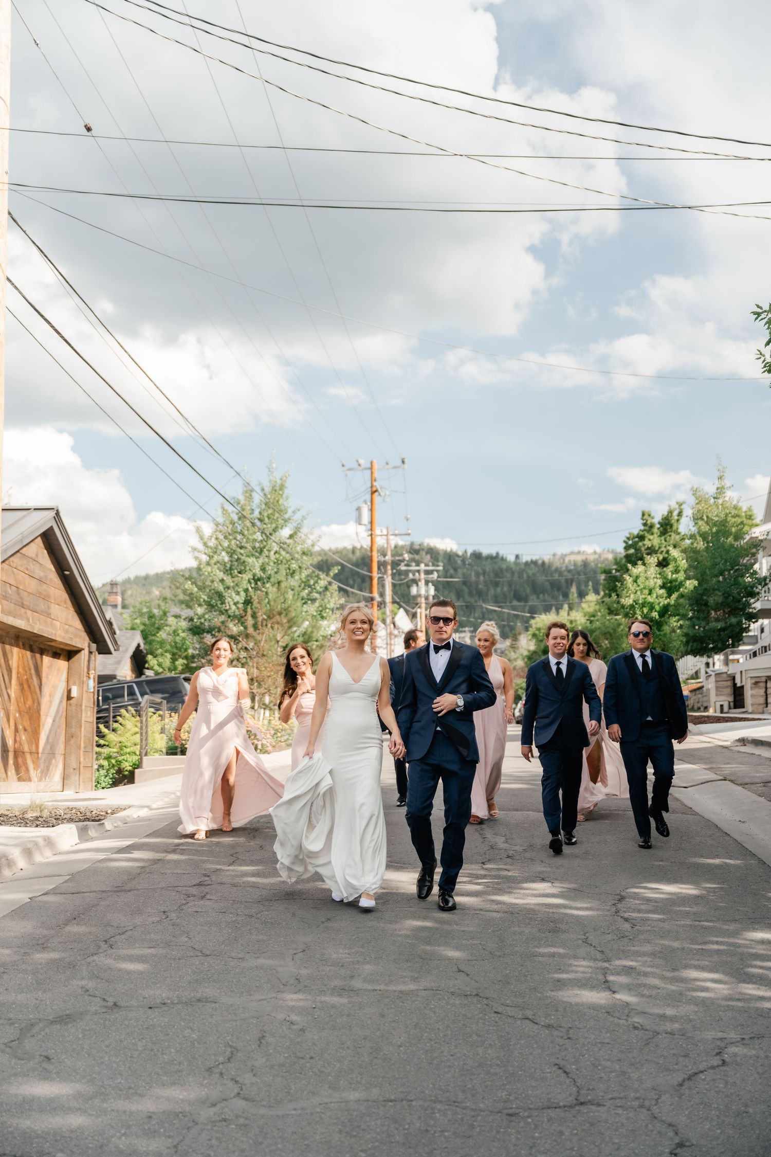 Wedding party walks together along an outdoor path with power lines and buildings in the background.