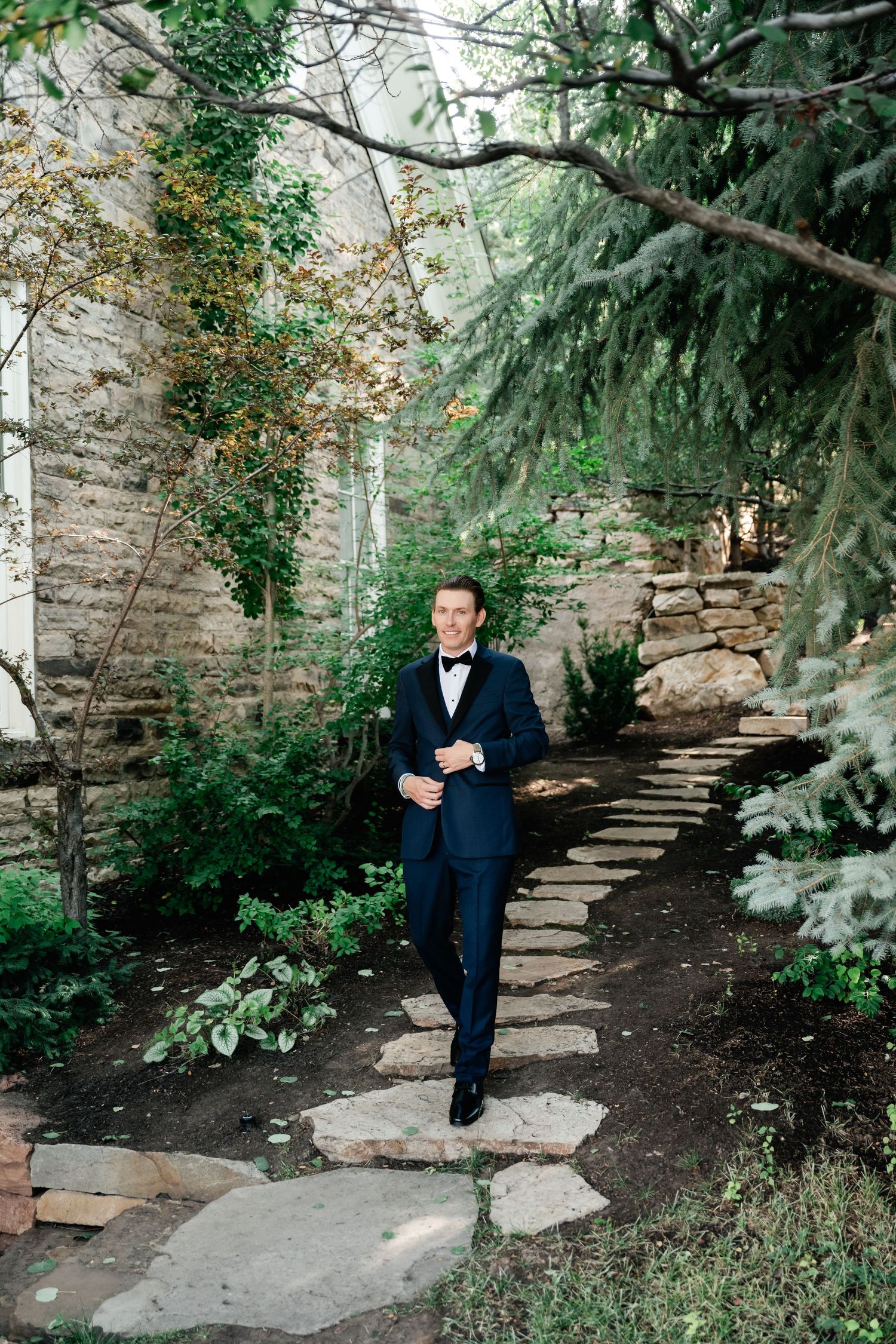 A stone path winds through a lush garden setting with evergreen trees and natural landscaping.