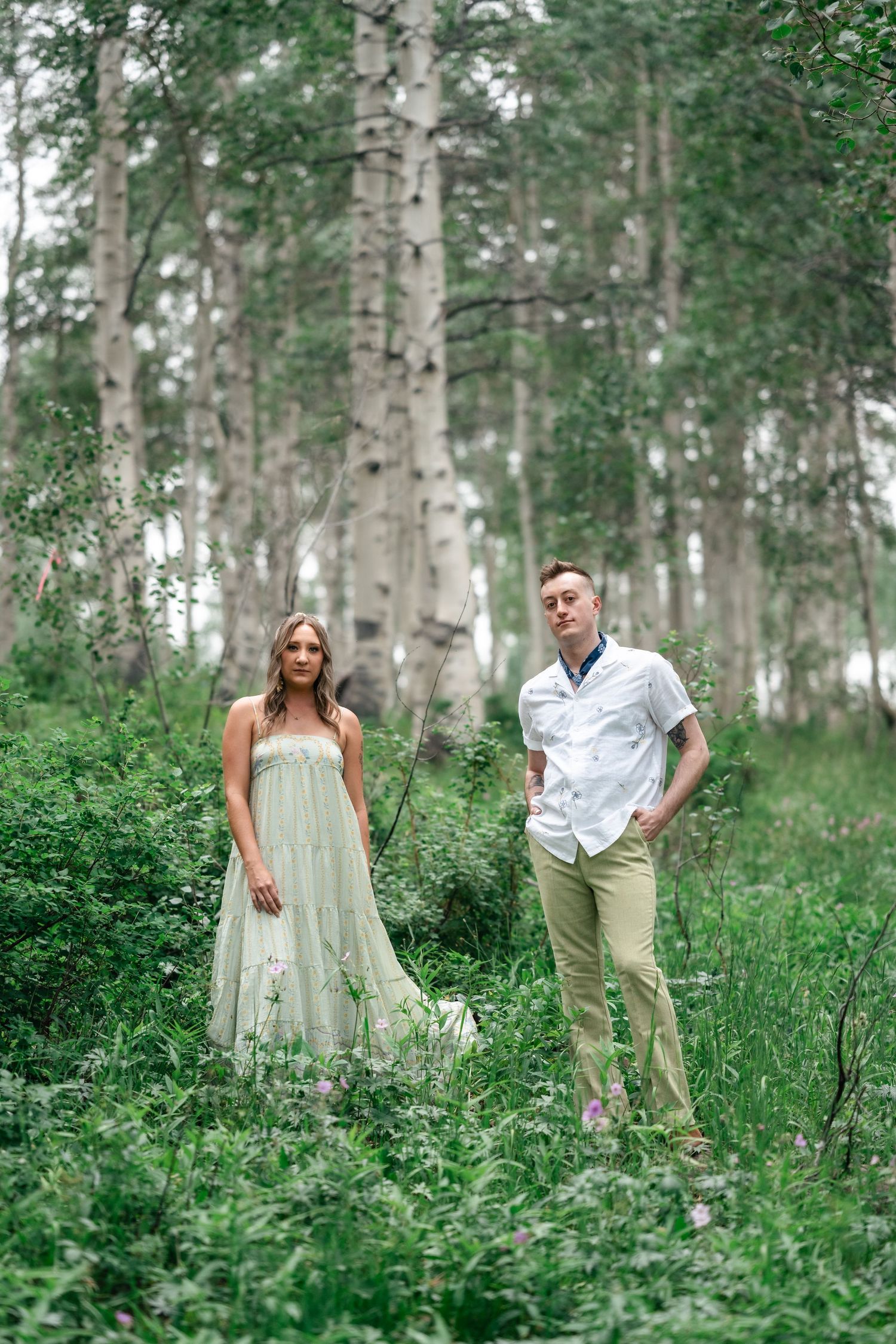 A couple walks through a serene aspen grove with sunlight filtering through the white bark trees.
