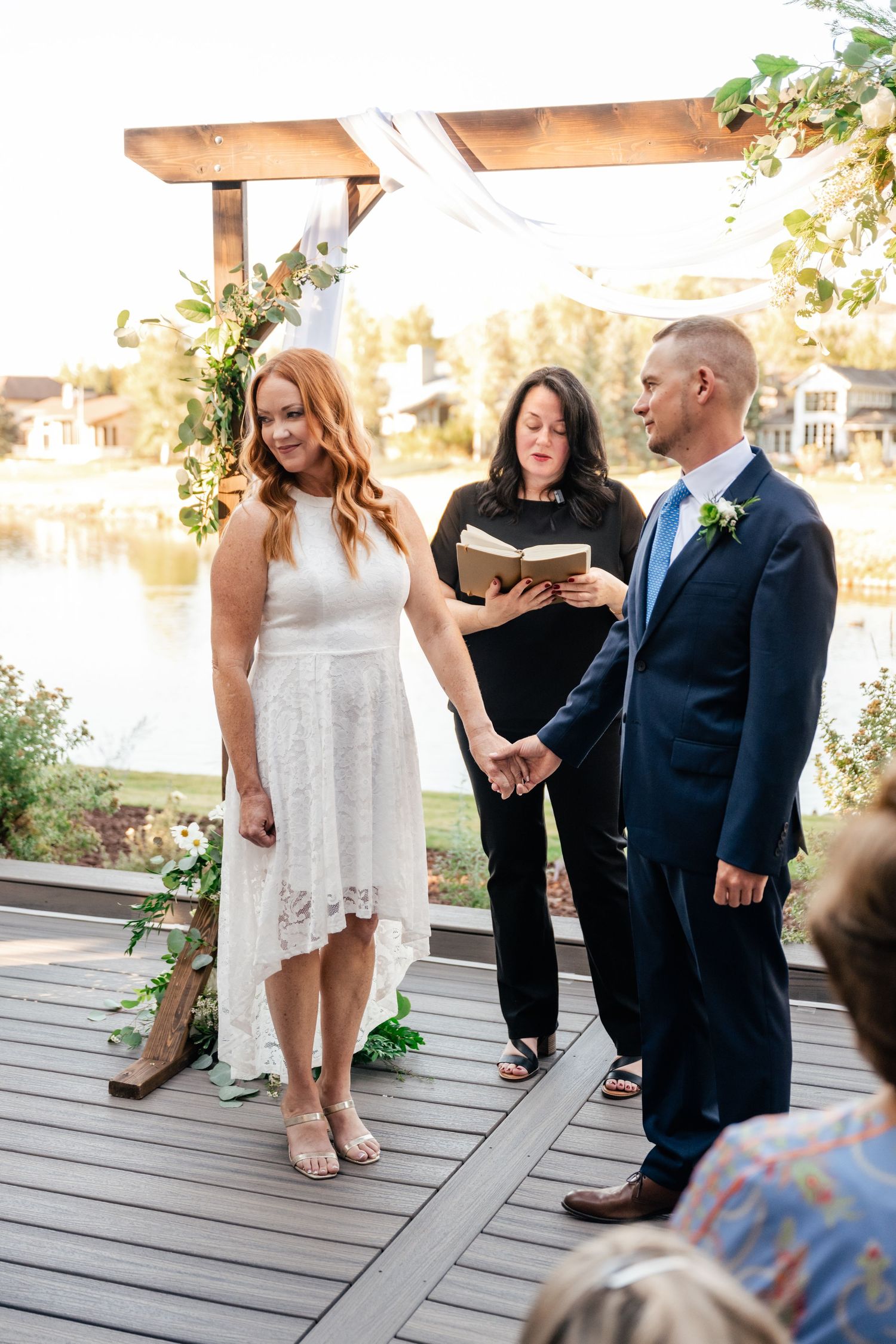 A group gathers on a wooden deck during a wedding ceremony at sunset.