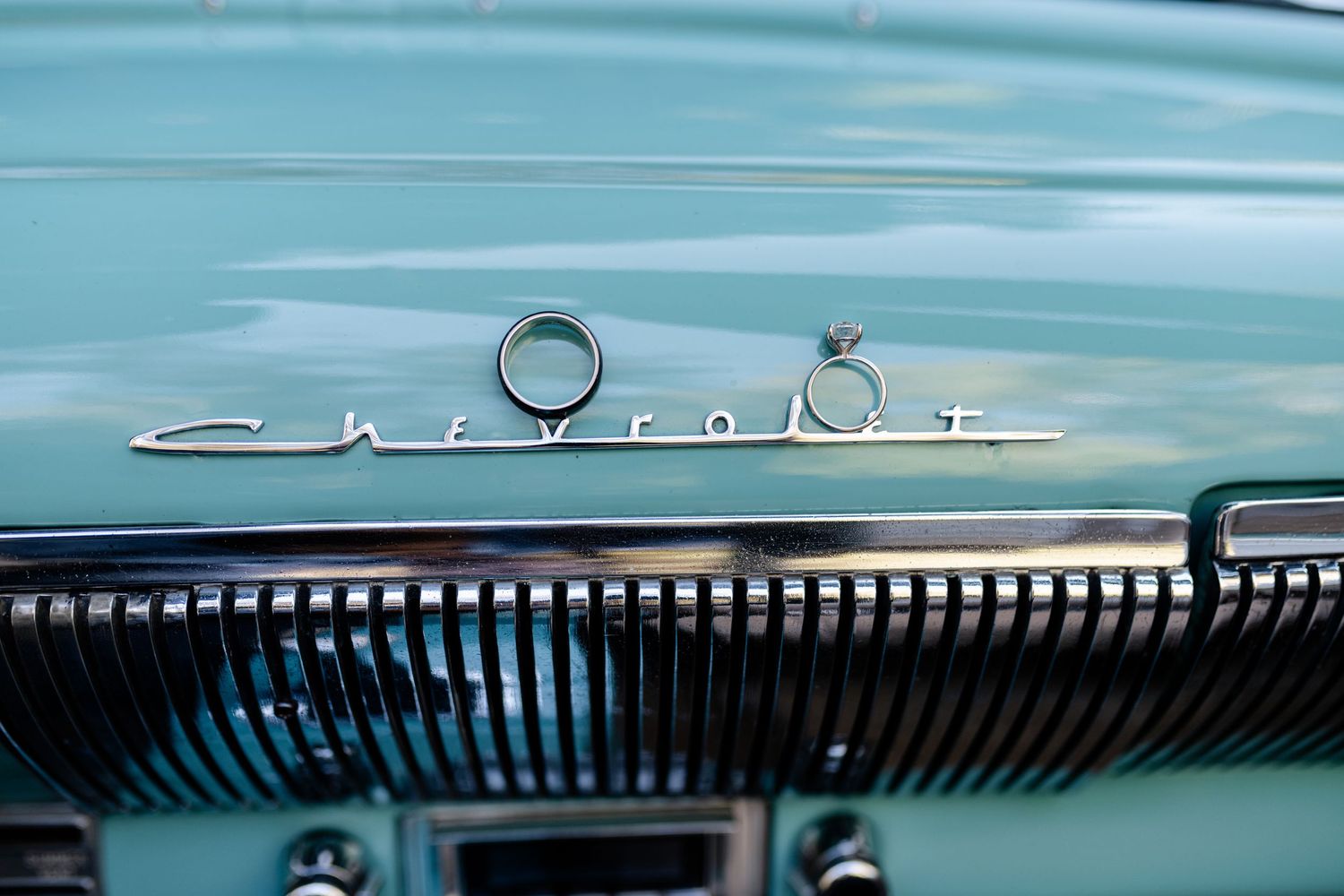 Close-up view of a vintage Chevrolet chrome emblem and grille on a turquoise classic car.