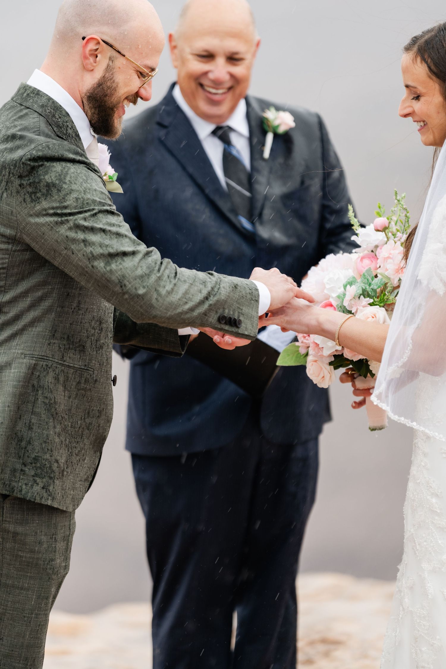 A joyful wedding ceremony moment captured outdoors as rings are exchanged with an officiant present.