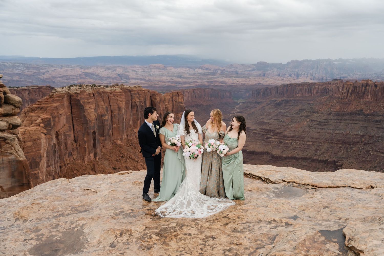 Wedding ceremony group gathers at majestic canyon overlook with vast desert landscape behind them.
