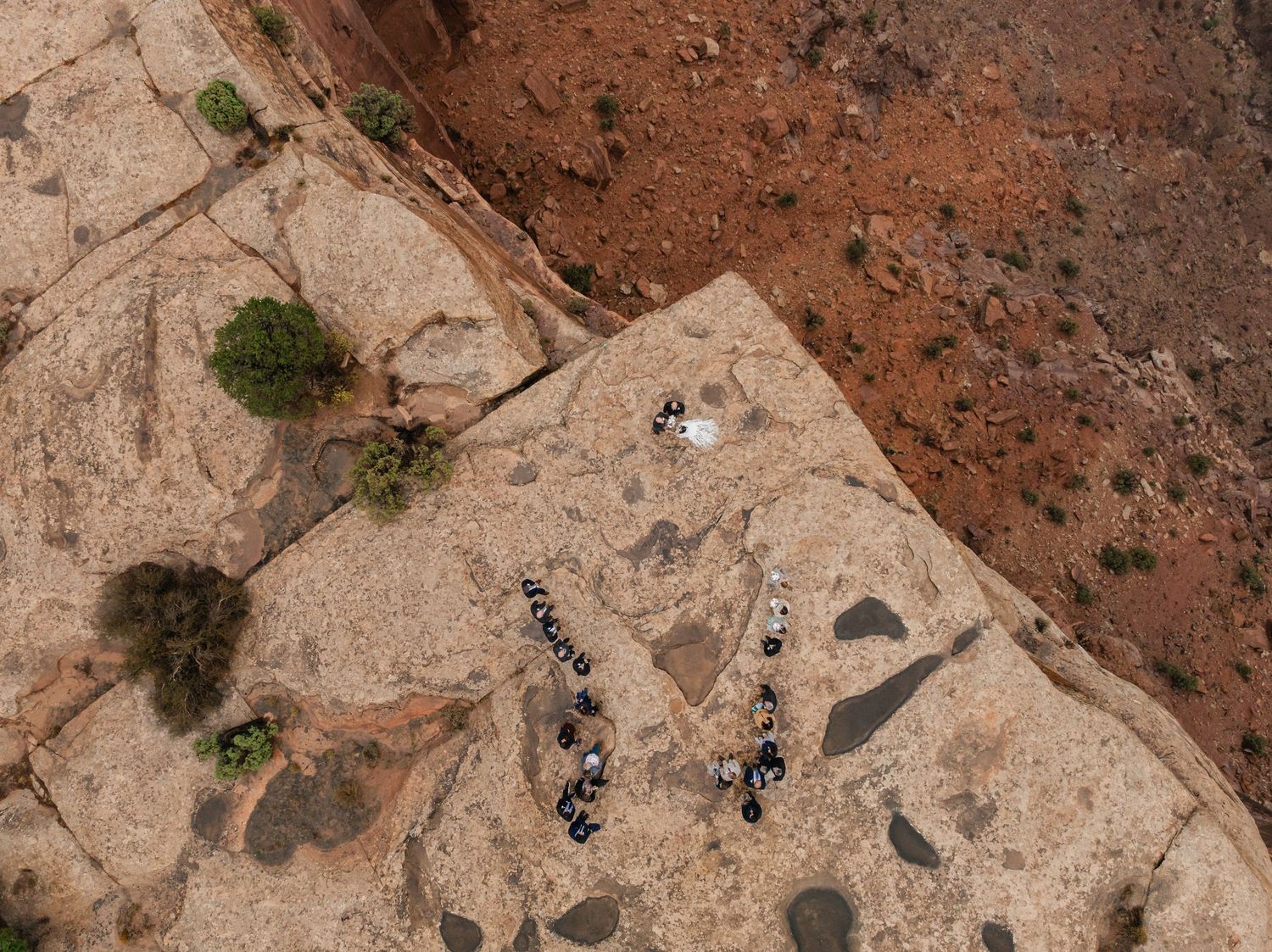 Aerial view of mountain bikers riding along a winding dirt trail through red desert terrain.