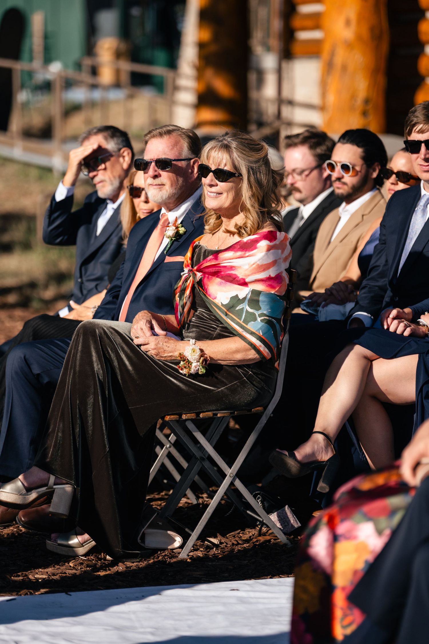 Wedding guests in formal attire seated in rows of folding chairs during an outdoor ceremony at sunset.