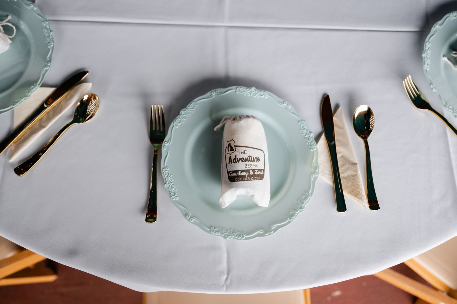 Elegant place settings with mint green plates and vintage silverware arranged on a light gray tablecloth.