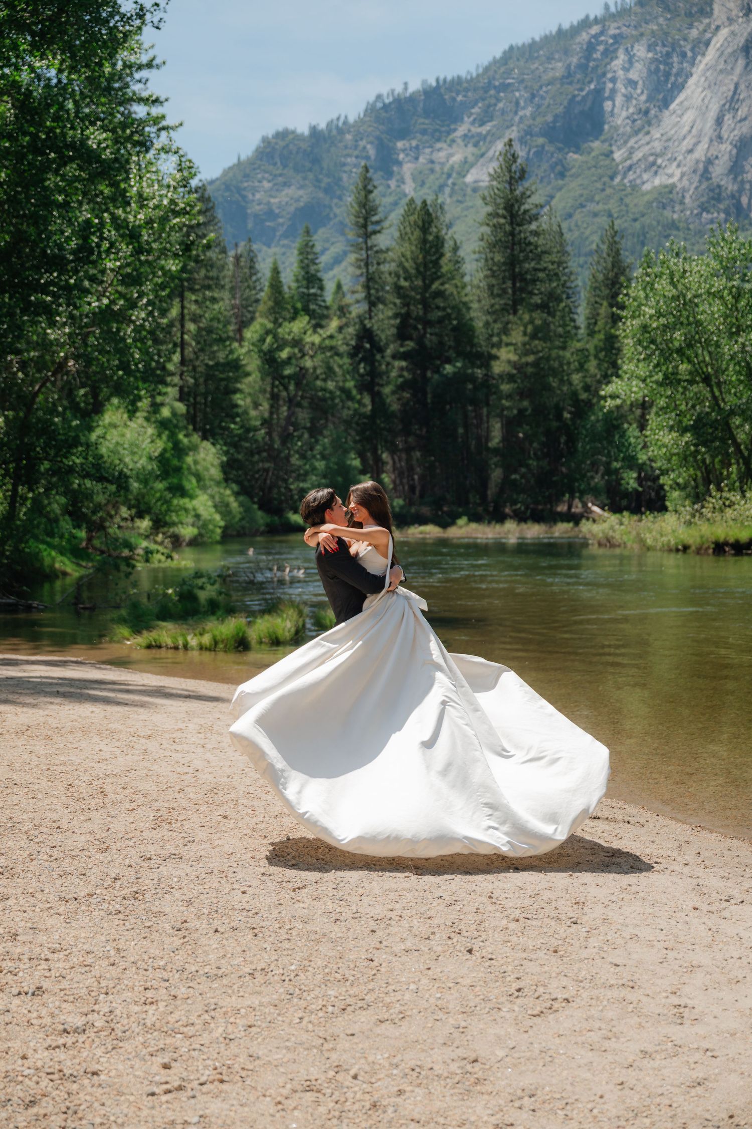 Bride and groom dancing by a river with mountain and pine trees backdrop at Yosemite wedding.