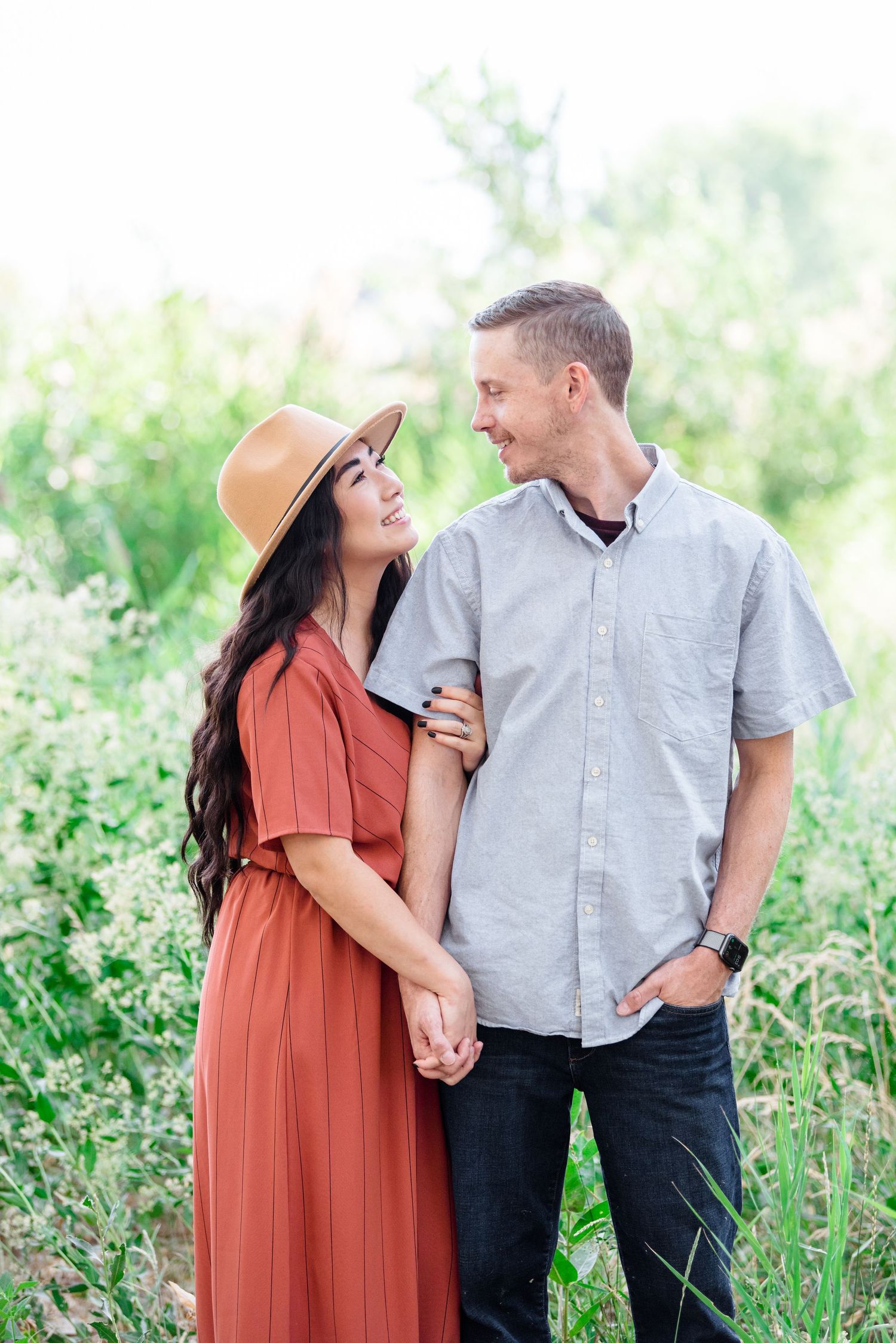 Couple in casual attire sharing a loving moment in a sunny wildflower field.