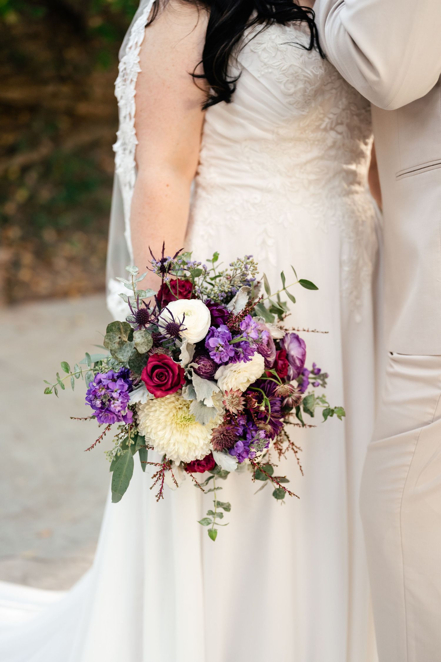A stunning bridal bouquet featuring deep red roses, purple flowers, and white dahlias with cascading greenery.