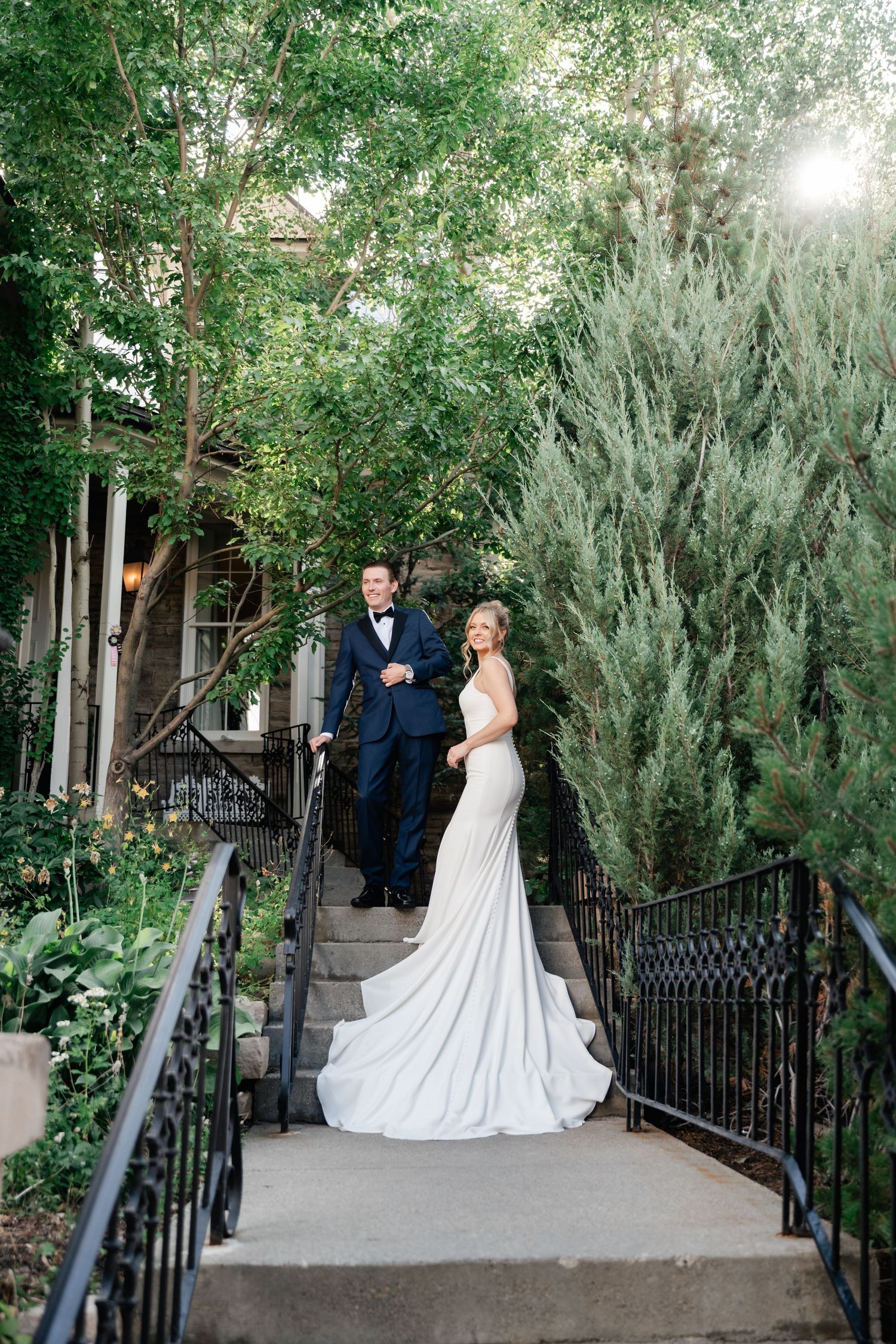 A romantic garden wedding scene with a couple in formal attire standing on a path surrounded by lush greenery and trees. Park City Wedding.