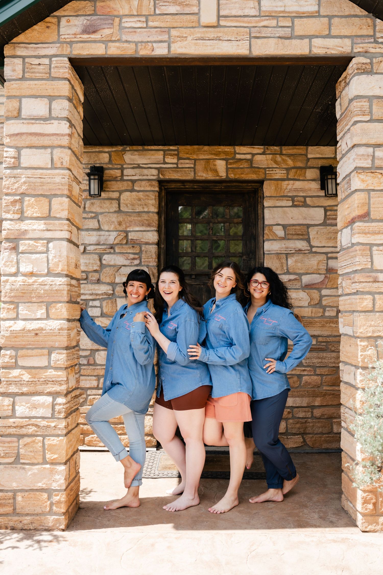 Group wearing matching blue shirts pose playfully on a stone porch.