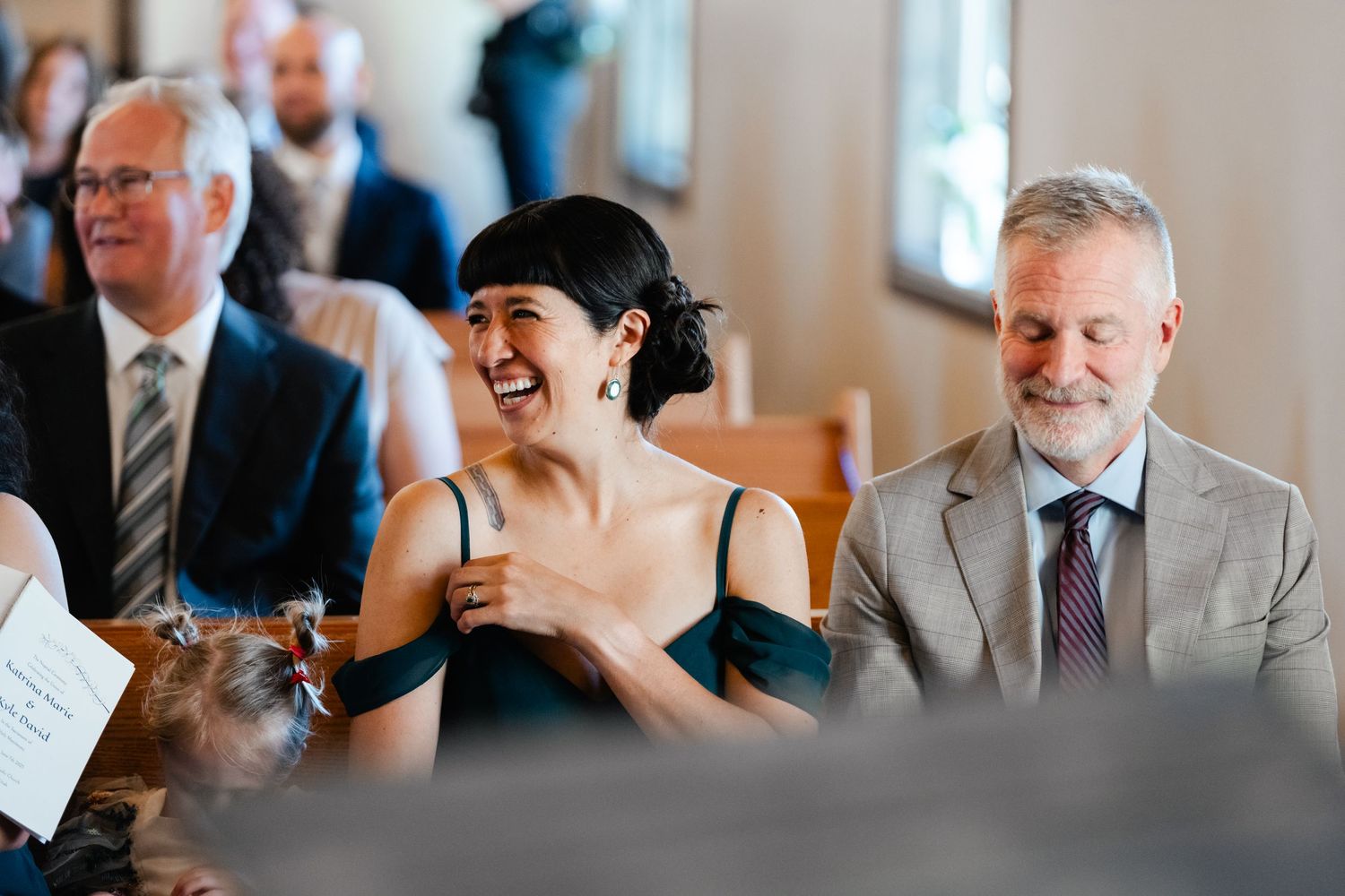 Wedding guests smile and react during ceremony in elegant church setting.