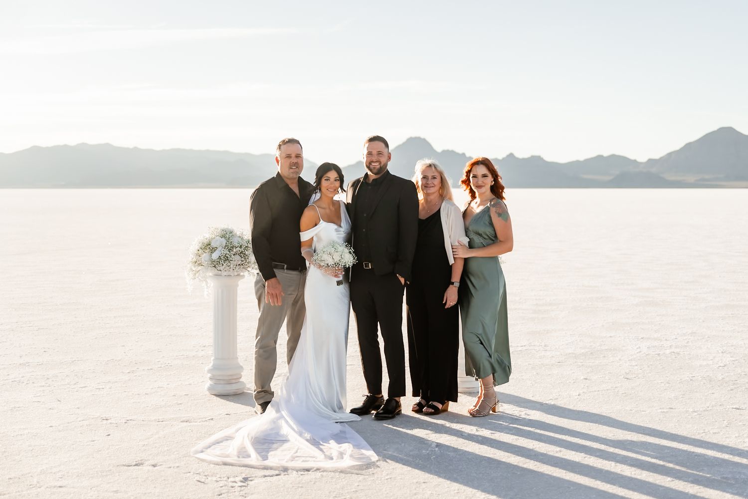 Wedding party gathering on bright white salt flats with mountains in the distance.