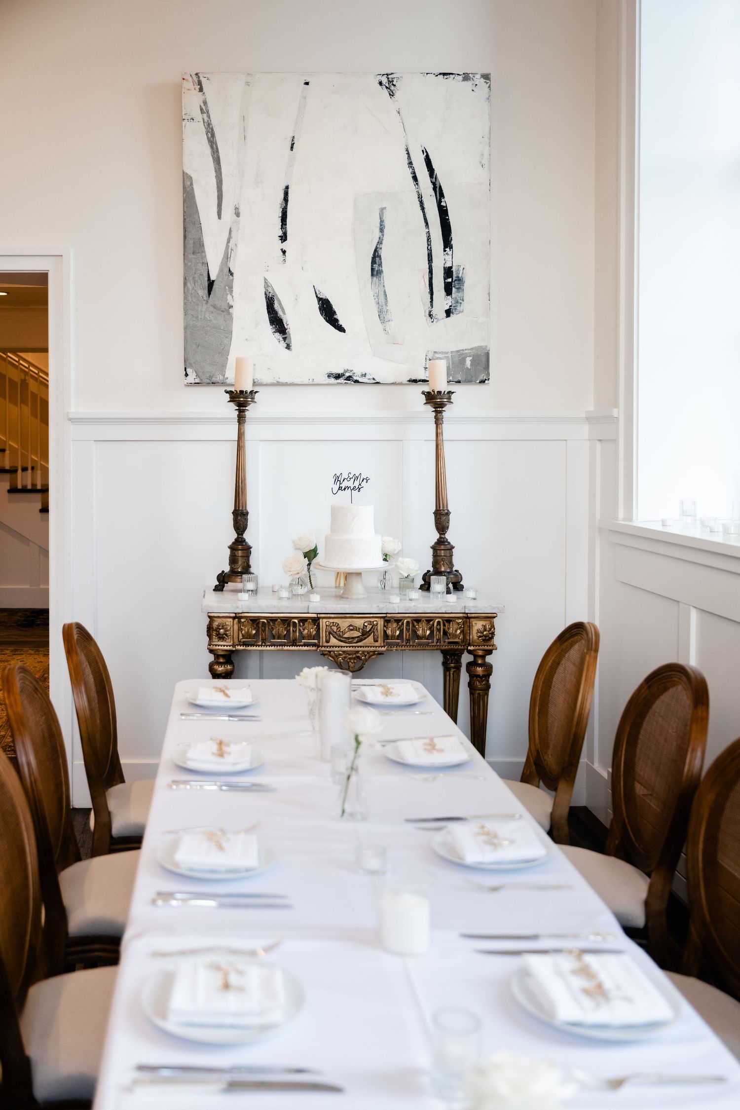 Elegant white dining table setup with classic place settings and abstract artwork on the wall.