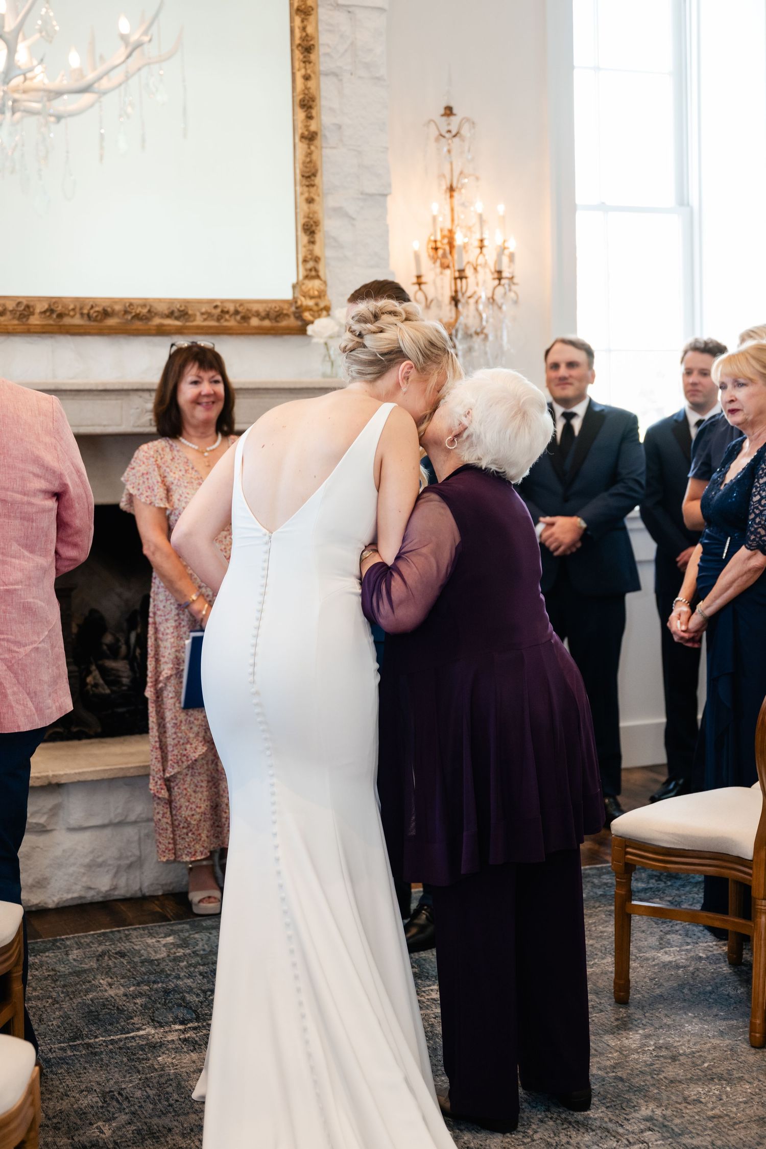 Wedding ceremony in an elegant white room with vintage fireplace and chandelier.