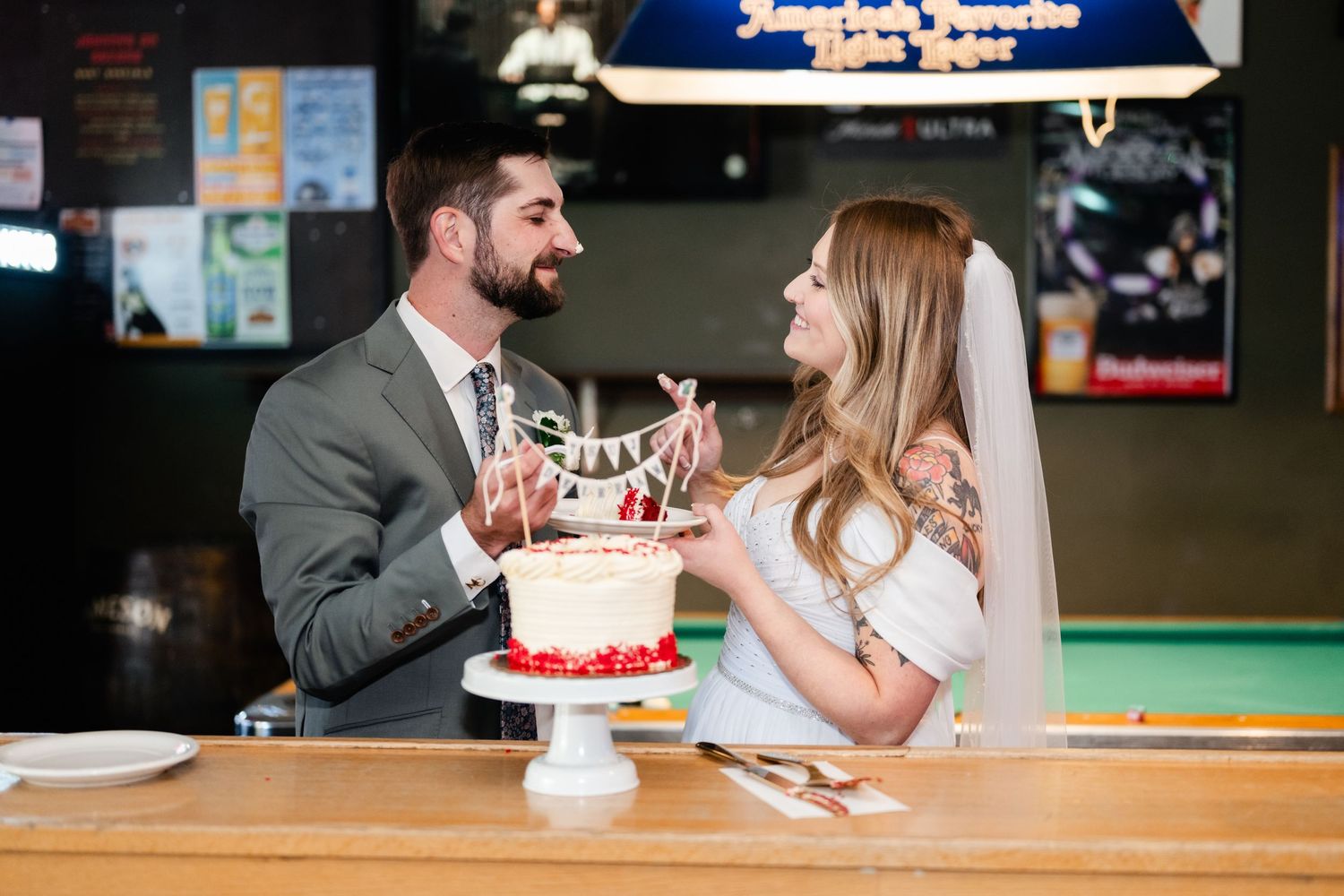 A couple shares their wedding cake at a casual bar reception.