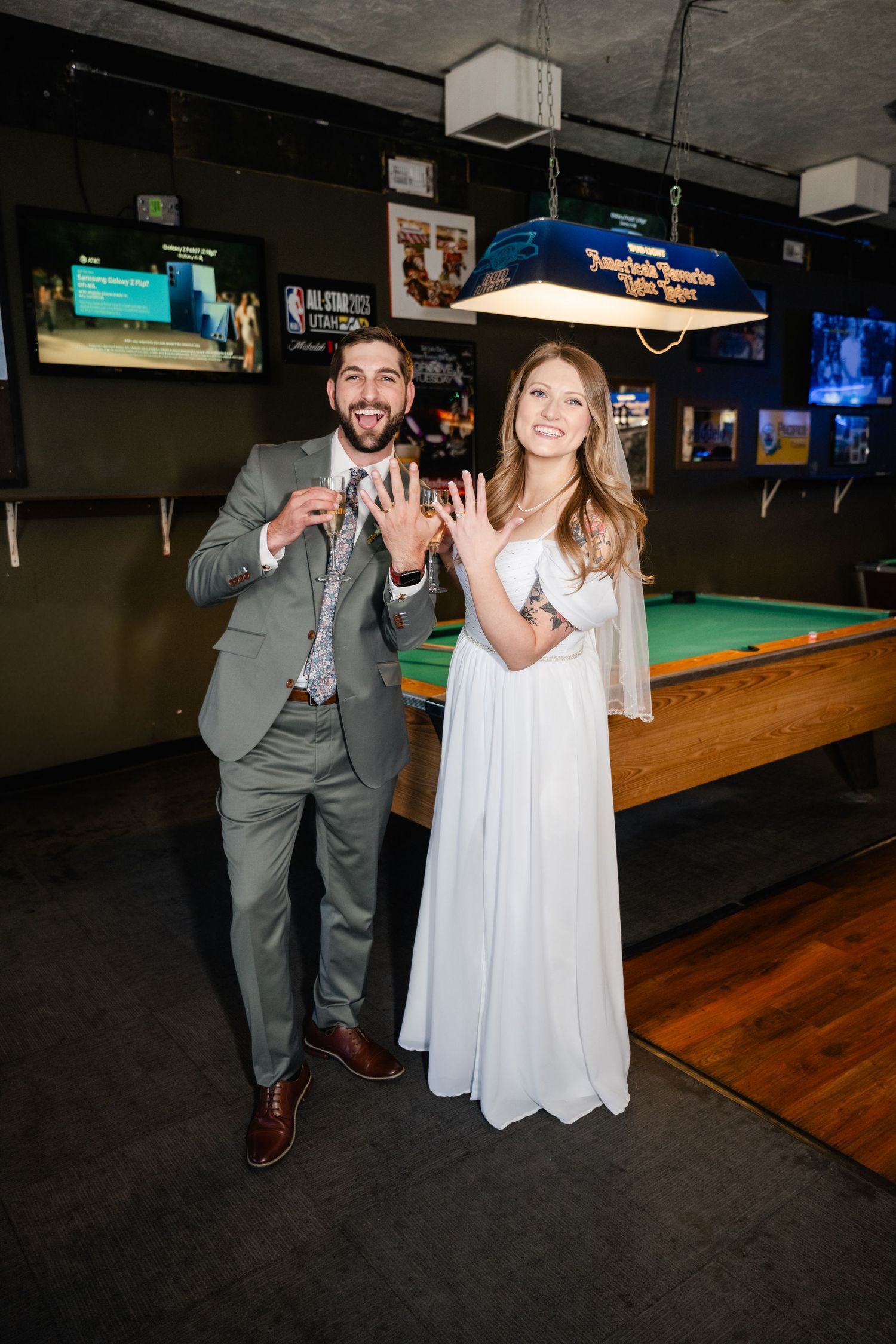 A formal couple poses playfully by a pool table in a bar setting.
