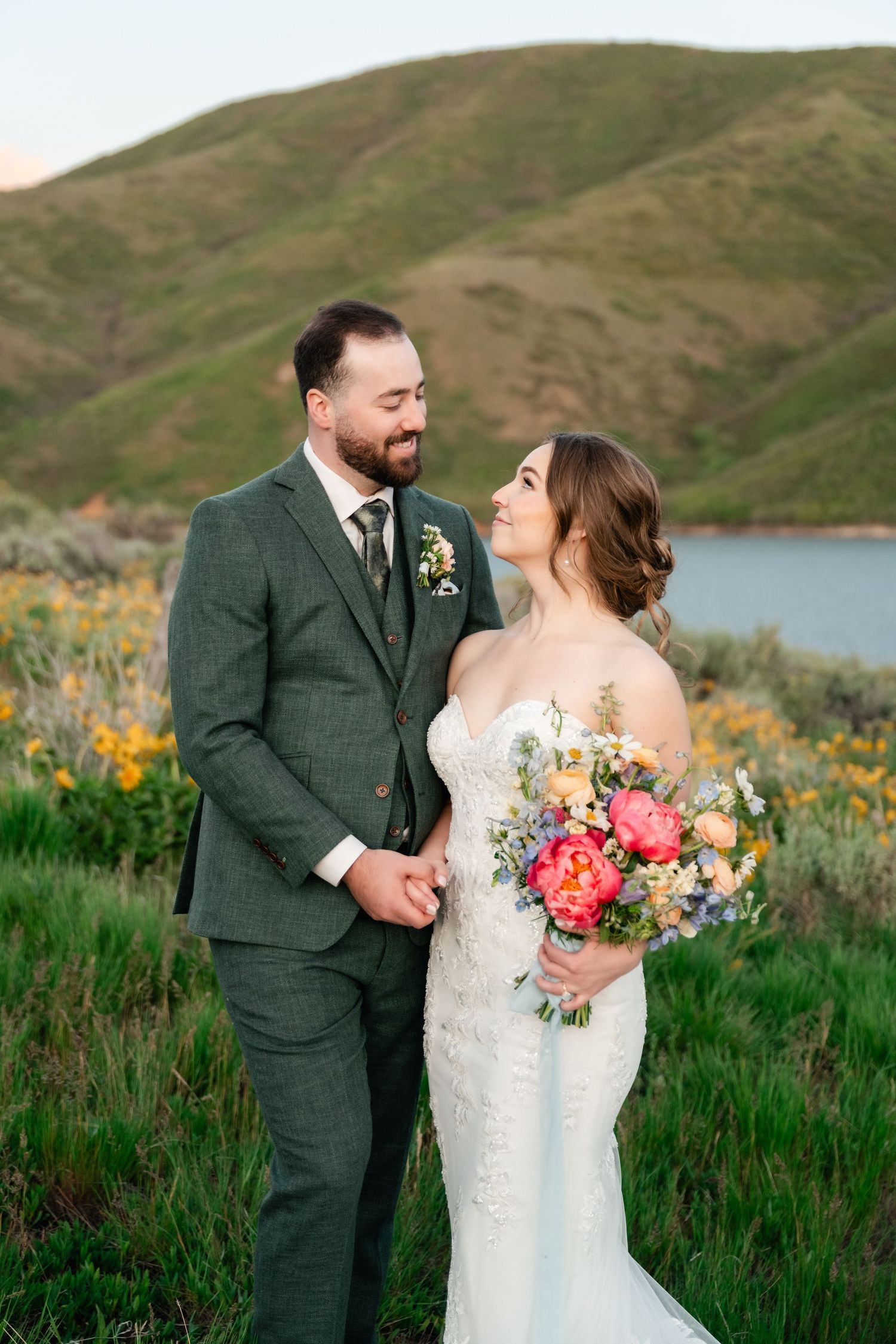 A newlywed couple shares an intimate moment surrounded by yellow wildflowers and mountain scenery.