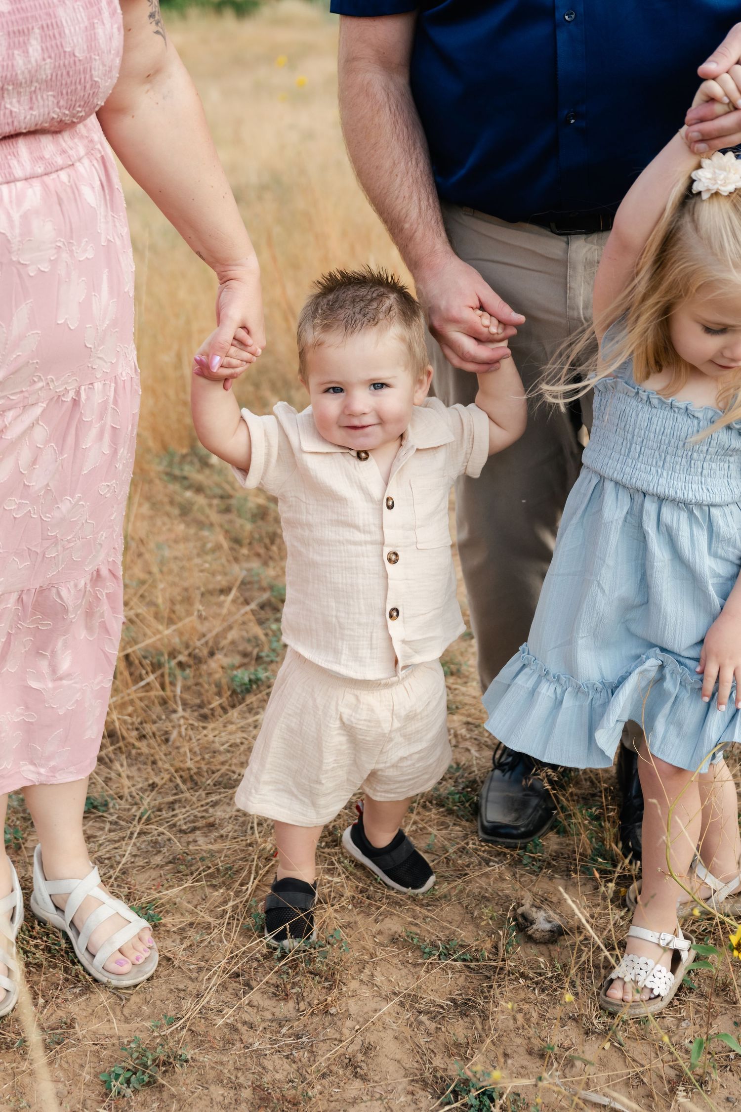 Family holding hands while walking together on a dirt path in summer attire.
