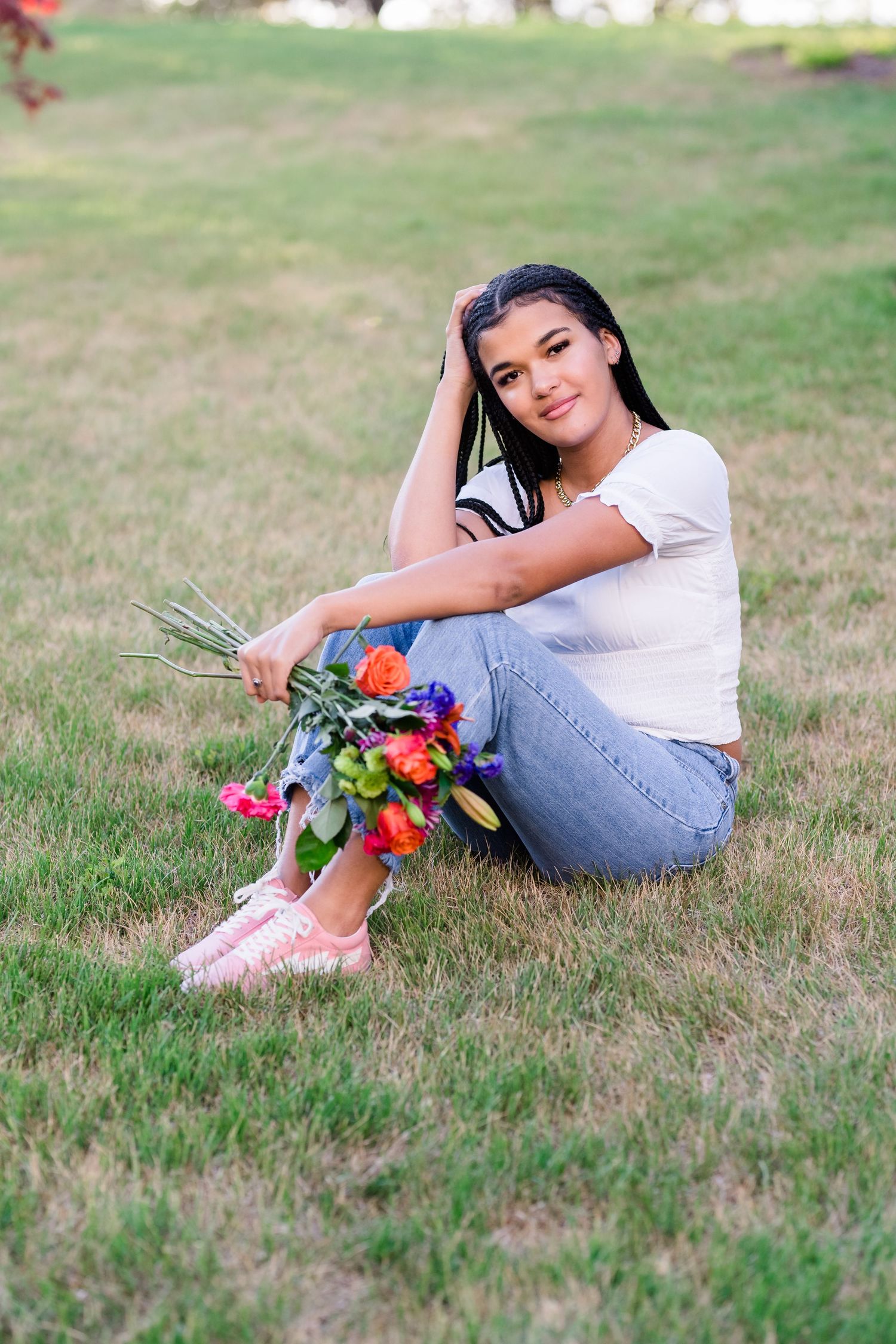 Person in casual white top and jeans reclines on grass holding colorful flowers in outdoor portrait series.