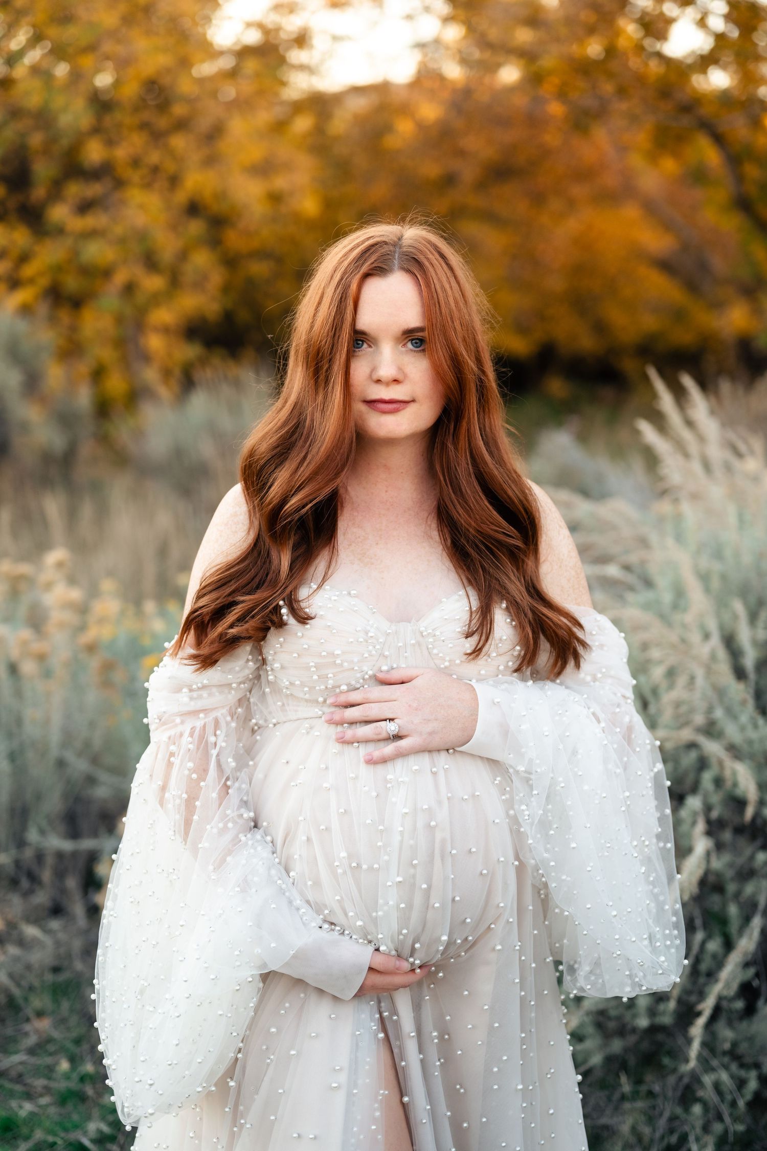 Ethereal maternity portraits in a white lace gown against warm fall foliage and sage brush backdrop.