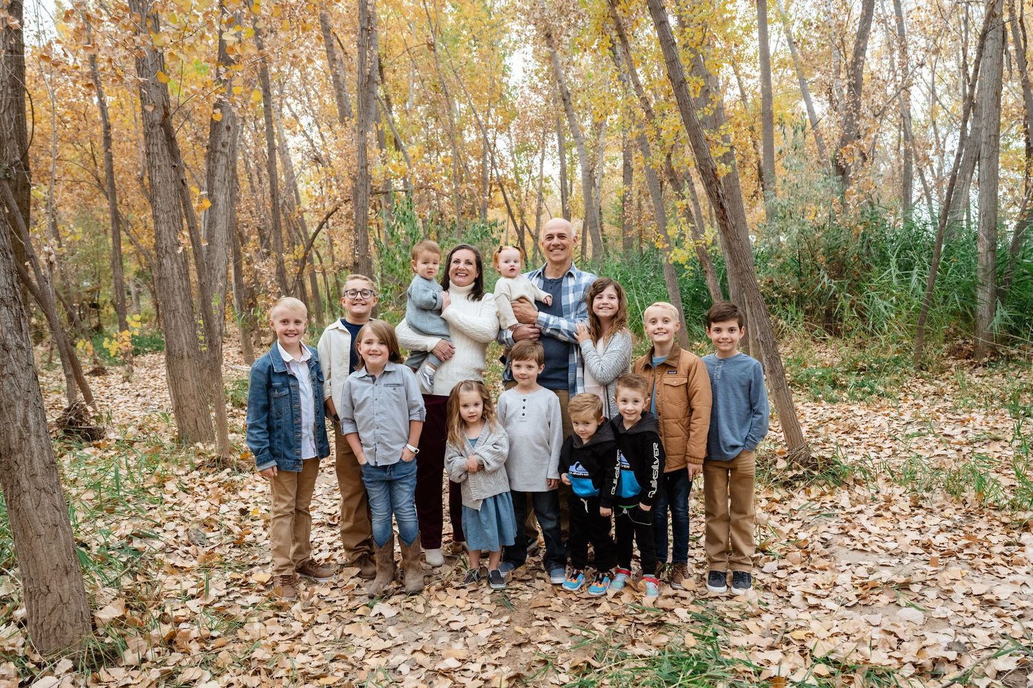 A group of people pose together in a wooded area with autumn leaves covering the ground during fall season.